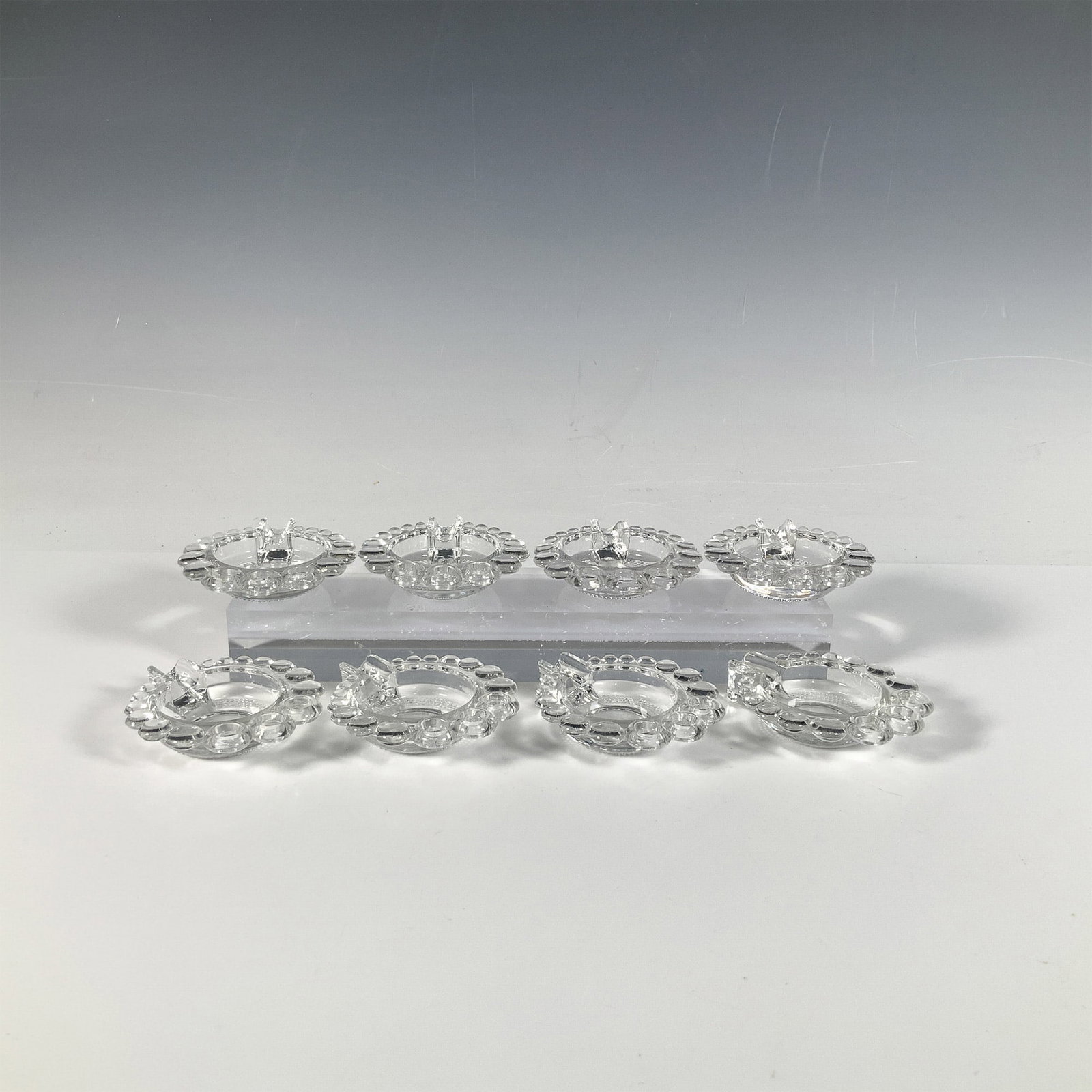 Set of 8 Duncan & Miller Glass Teardrop Ashtrays: This stunning collection includes eight small clear ashtrays with a single slot, adorned with a stacked bubble pattern. Each ashtray measures: 3.25"L x 3"W x 0.75"H. Issued: 1933-1955 Dimensions: See 