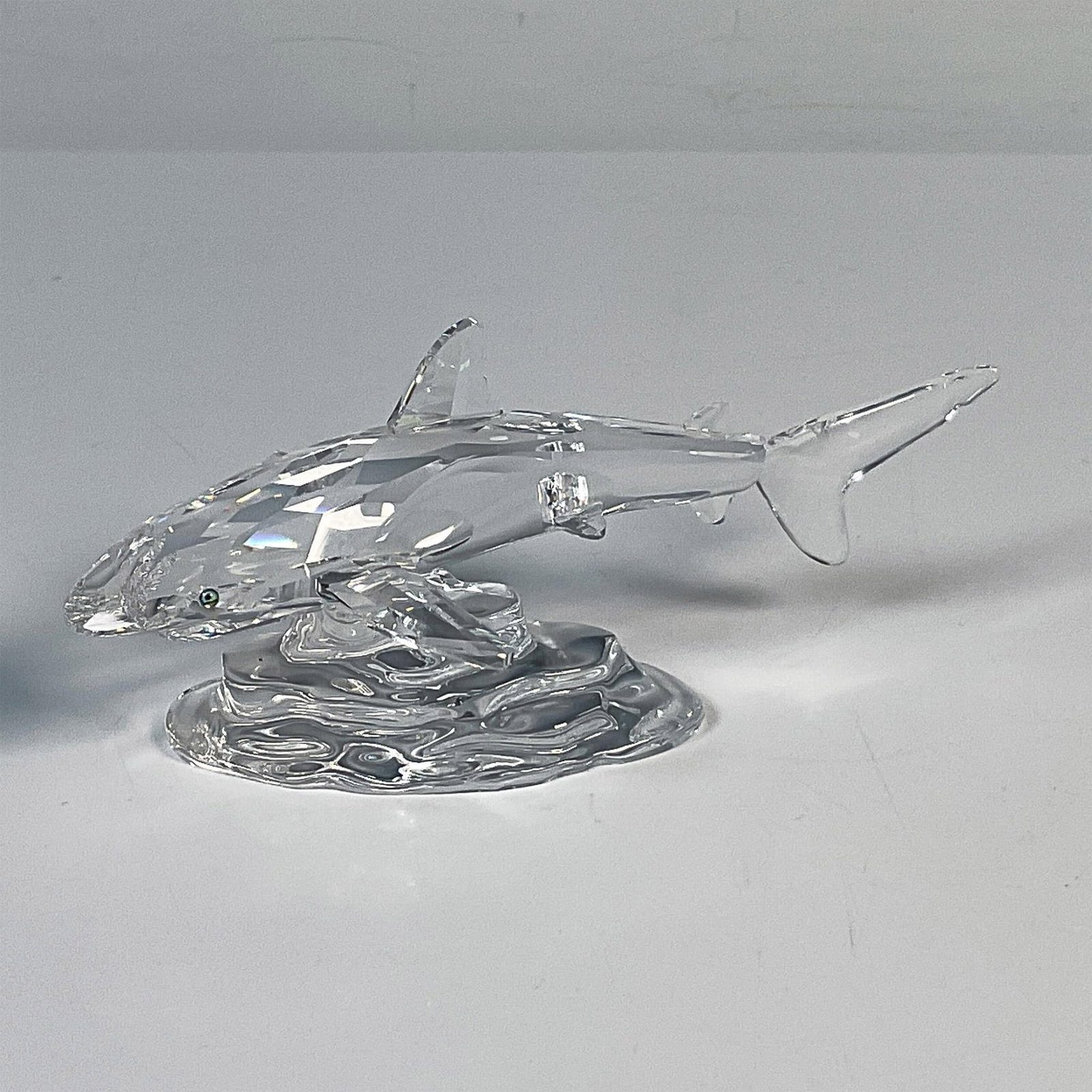 Swarovski Crystal Figurine, Baby Shark 269236: This baby shark was part of the South Sea grouping. The clear faceted crystal shark is skirting the bottom of the ocean, represented by a smooth crystal base. Swarovski etched backstamp. This item has