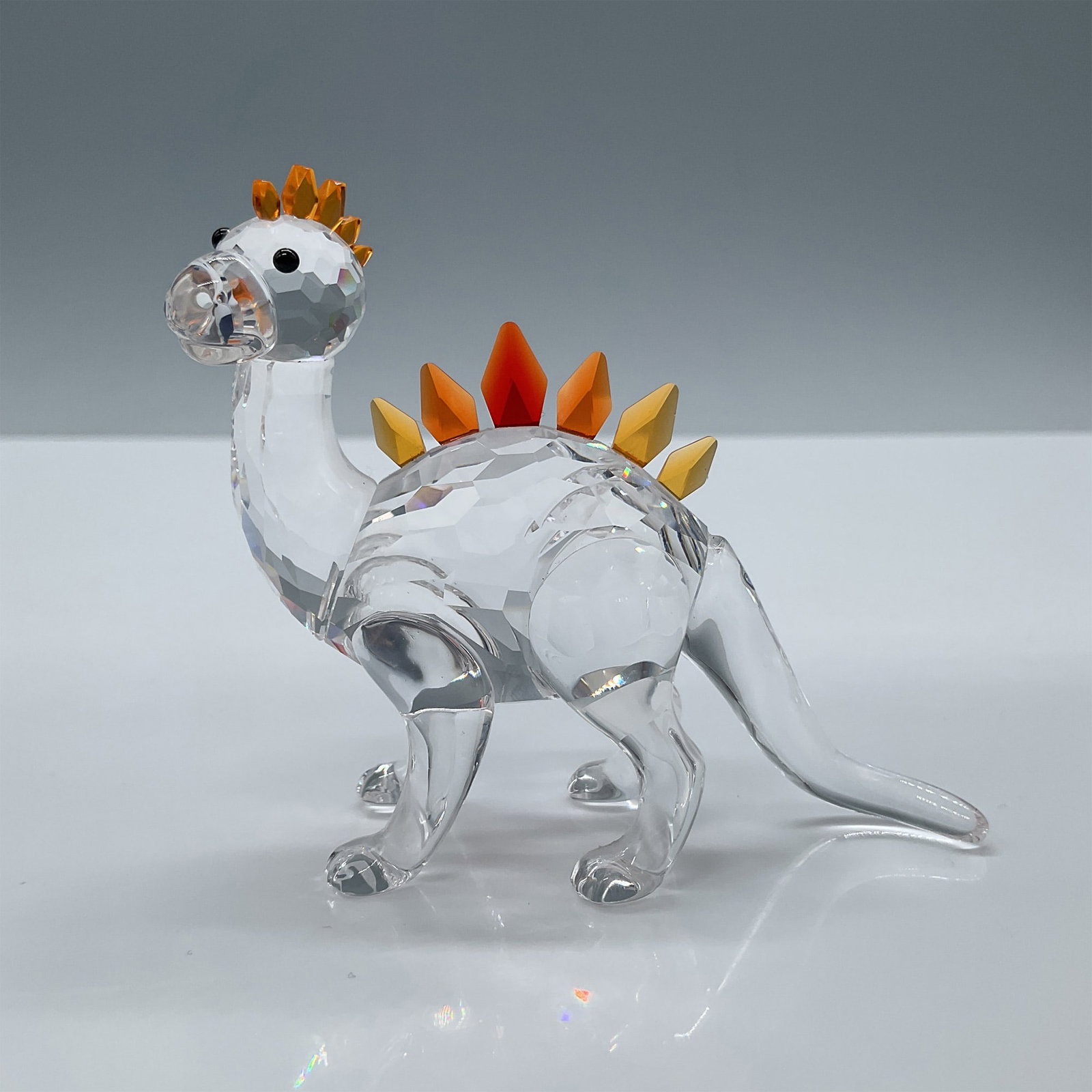 Swarovski Crystal Figurine, Dino Dinosaur: Part of the Fairy Tales collection. Features an adorable clear facetted crystal dinosaur with amber and red crystal comb. Swarovski etched backstamp. This item has its original box. Box measures: 4.75