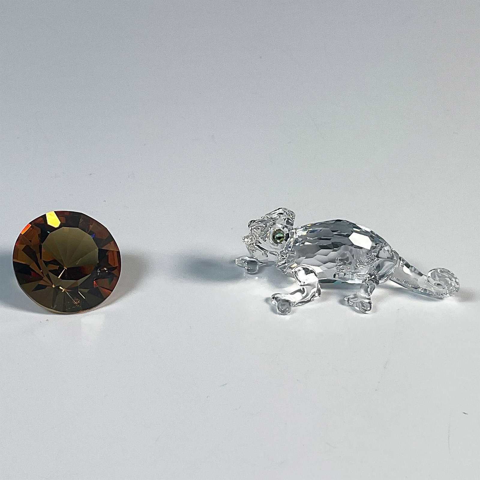 2pc Swarovski Crystal Figurine, Chameleon + Color Chaton: This clear crystal chameleon was a member of the Rare Encounters grouping. His body is made from a clear faceted crystal with green eyes. The chameleon measures 2"L x 1"W x 0.75"H. The chaton is an am