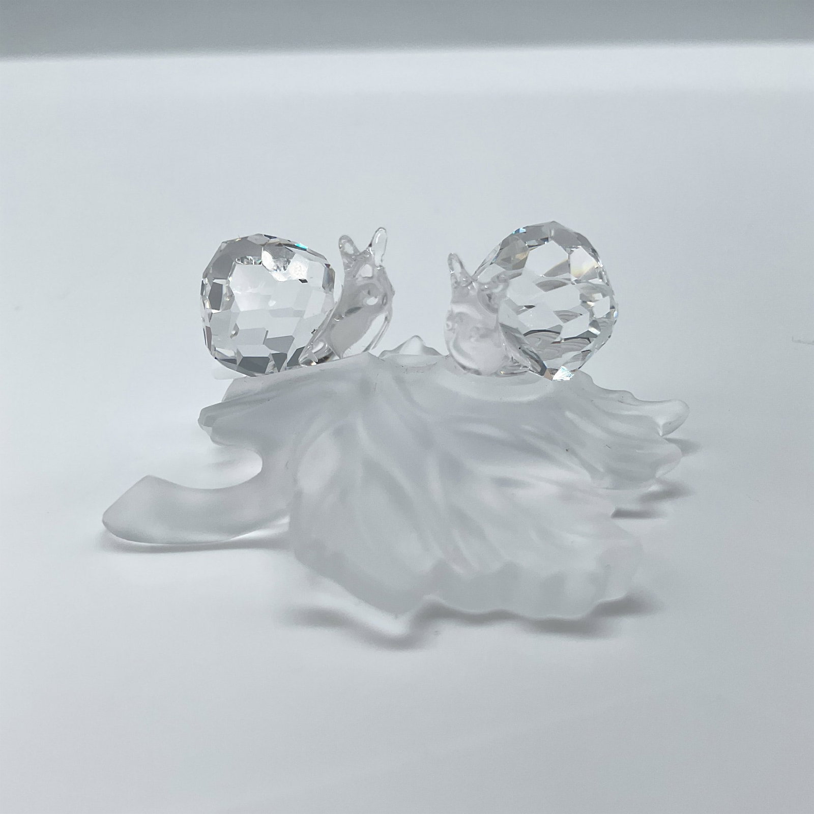 Swarovski Crystal Figurine, Snail Babies on Vine Leaf: Part of the In The Secret Garden collection. An adorable and whimsical piece of two clear snails on a frosted leaf. Swarovski etched mark. This item has its original box, box dimensions: 3.5''L x 3.5'