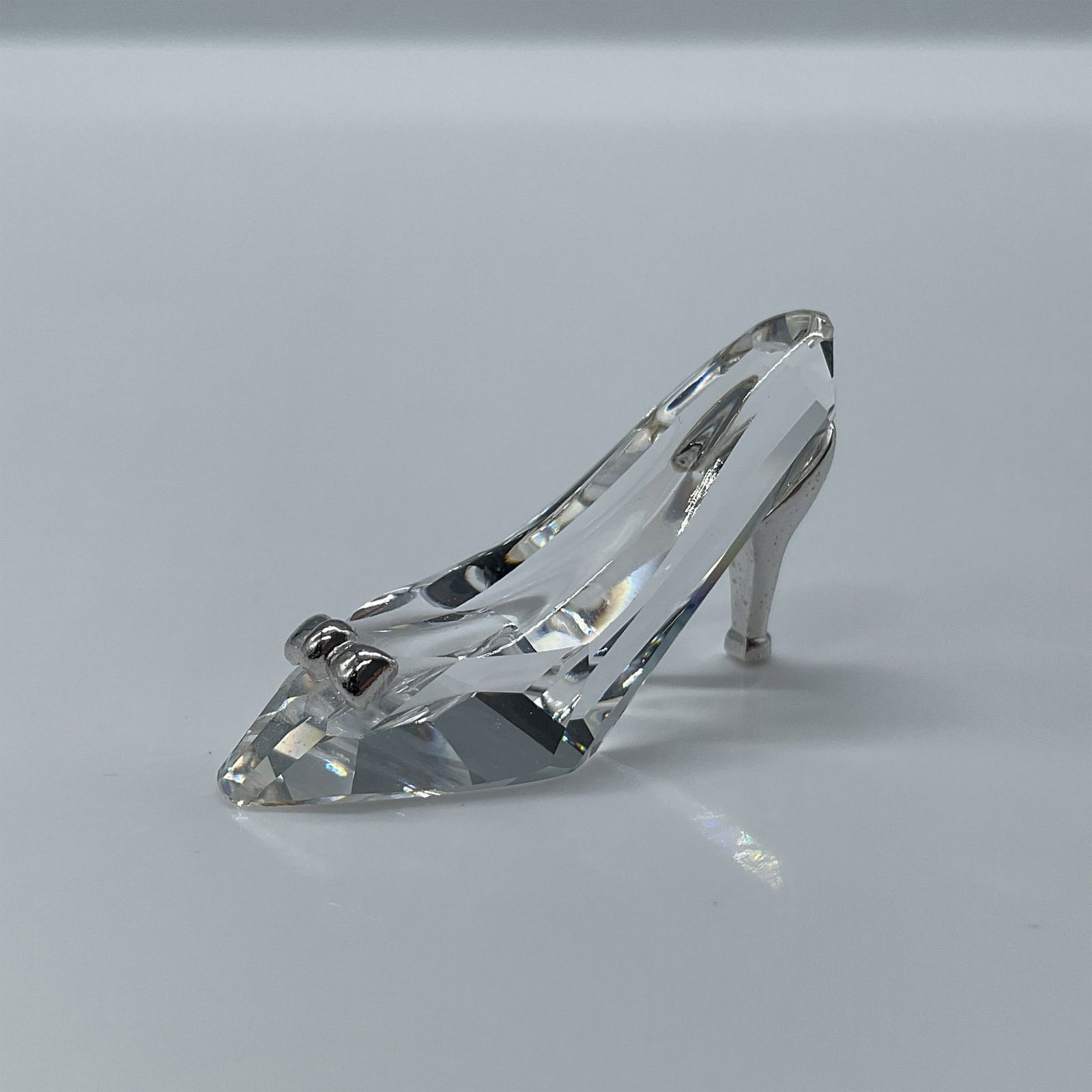 Swarovski Crystal Figurine, High-Heeled Shoe: Clear faceted crystal mini figure of a high-heeled shoe with a rhodium heel and bow. Swarovski etched backstamp. This item has its original box. Box measures: 2.5''L x 2.5''W x 1.5''H. Artist: Anton H