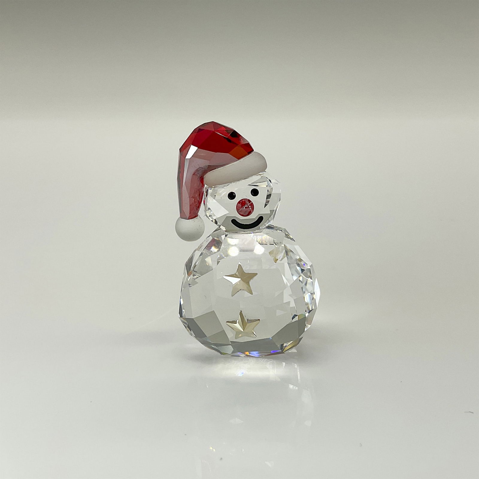 Swarovski Crystal Figurine, Rocking Snowman: Adorable clear crystal smiling snowman figure with red accents on its cap and nose. Swarovski swan mark. This item includes an original box: 1"L x 0.75"W x 1.5"H. Artist: Verena Castelein Issued: 2009