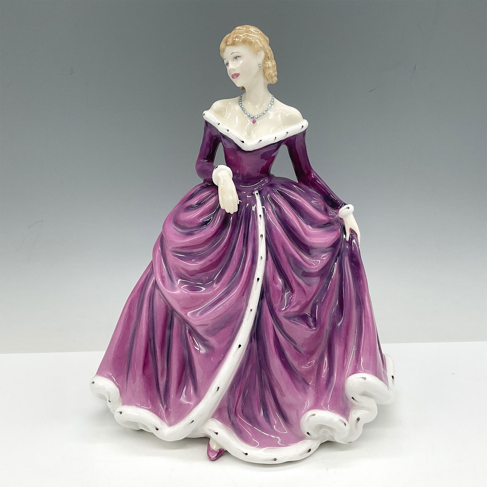 Royal Doulton Bone China Figurine, Belle HN4235: Part of the New Pretty Ladies series, lovely figure is dressed in purple gown trimmed in ermine. Royal Doulton backstamp. Artist: John Bromley Issued: 2001 - 2004 Dimensions: 7"L x 5.5"W x 8.5"H Count