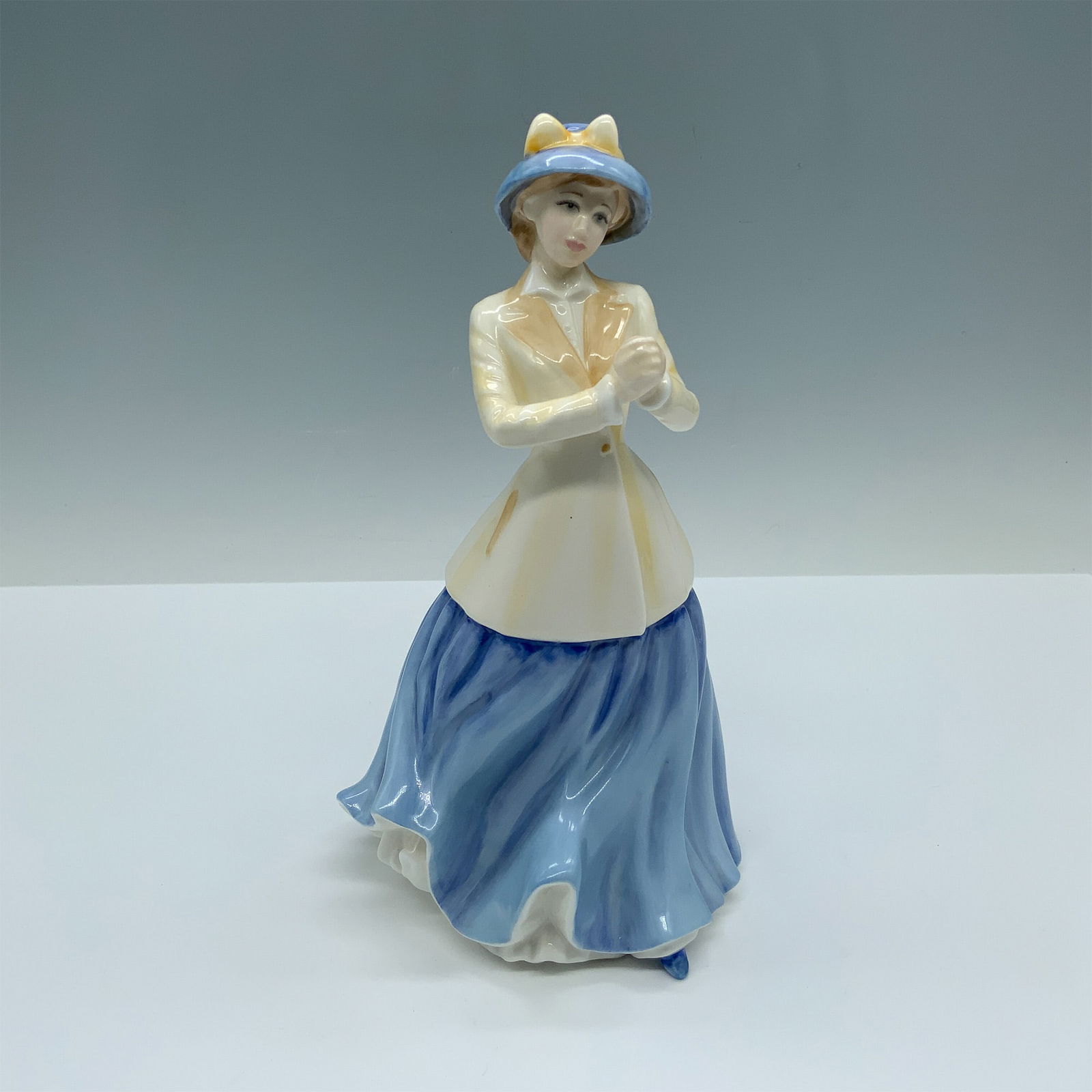 Royal Doulton Bone China Figurine, Hannah HN4407: Handmade and hand decorated glossy figure of a woman modeling a cream blazer over an azure blue skirt with a matching hat. Royal Doulton backstamp. Artist: Nada Pedley Issued: c. 2001 Dimensions: 4.5"