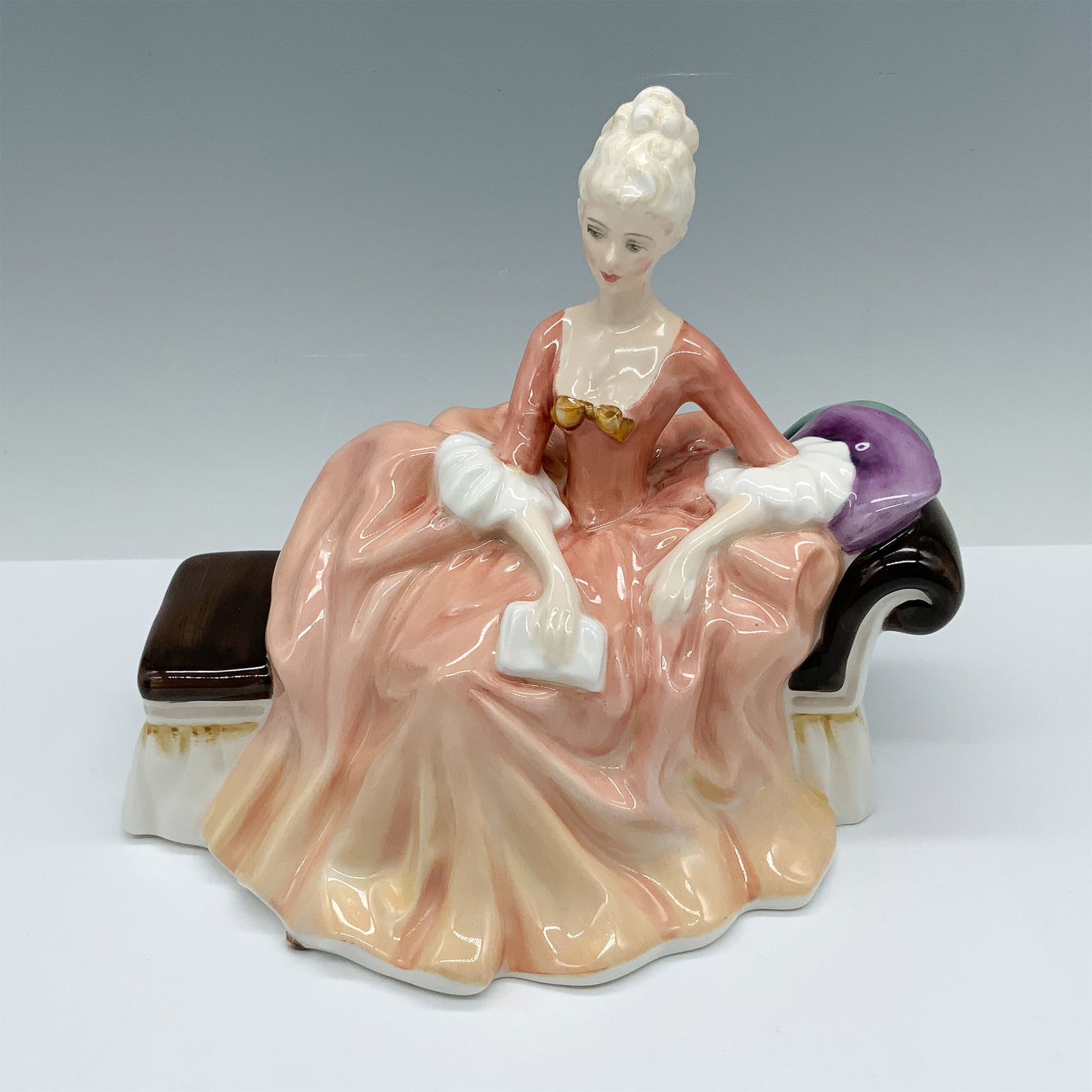Royal Doulton Bone China Figurine, Reverie HN2306: Handmade and hand decorated glossy figure of an elegant woman in a peach gown seated on a chaise. Royal Doulton backstamp. Artist: Peggy Davies Issued: c. 1963 Dimensions: 8"L x 5.5"W x 6.5"H Country