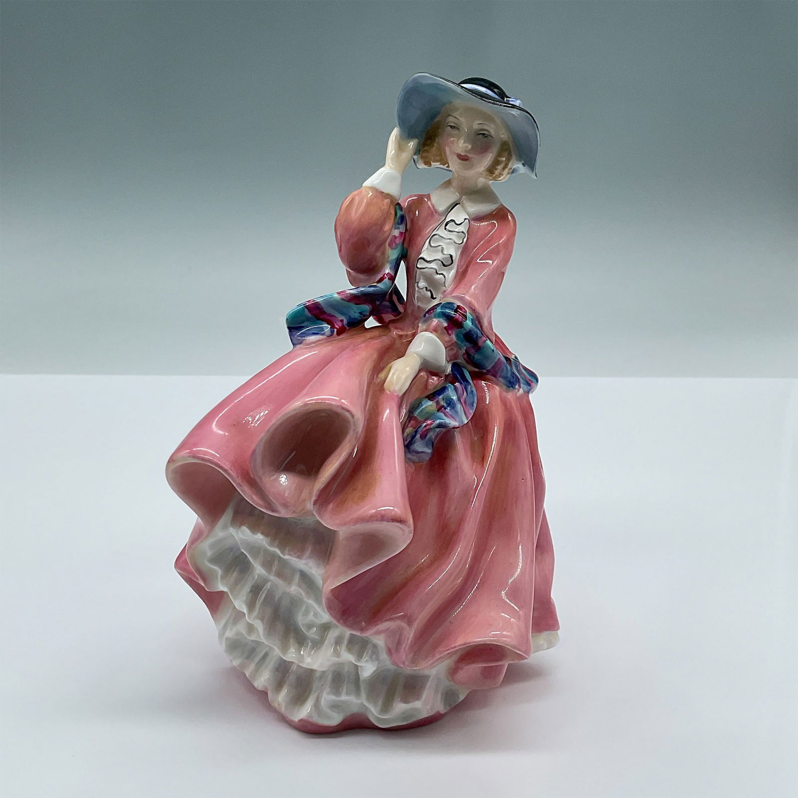 Royal Doulton Bone China Figurine, Top O The Hill HN1849: Delightful figure of a lady in a flowing pink dress, gracefully caught in the wind as she clings to her hat and gently holds her billowing dress. A part of the Harradine Classics series. Royal Doulton