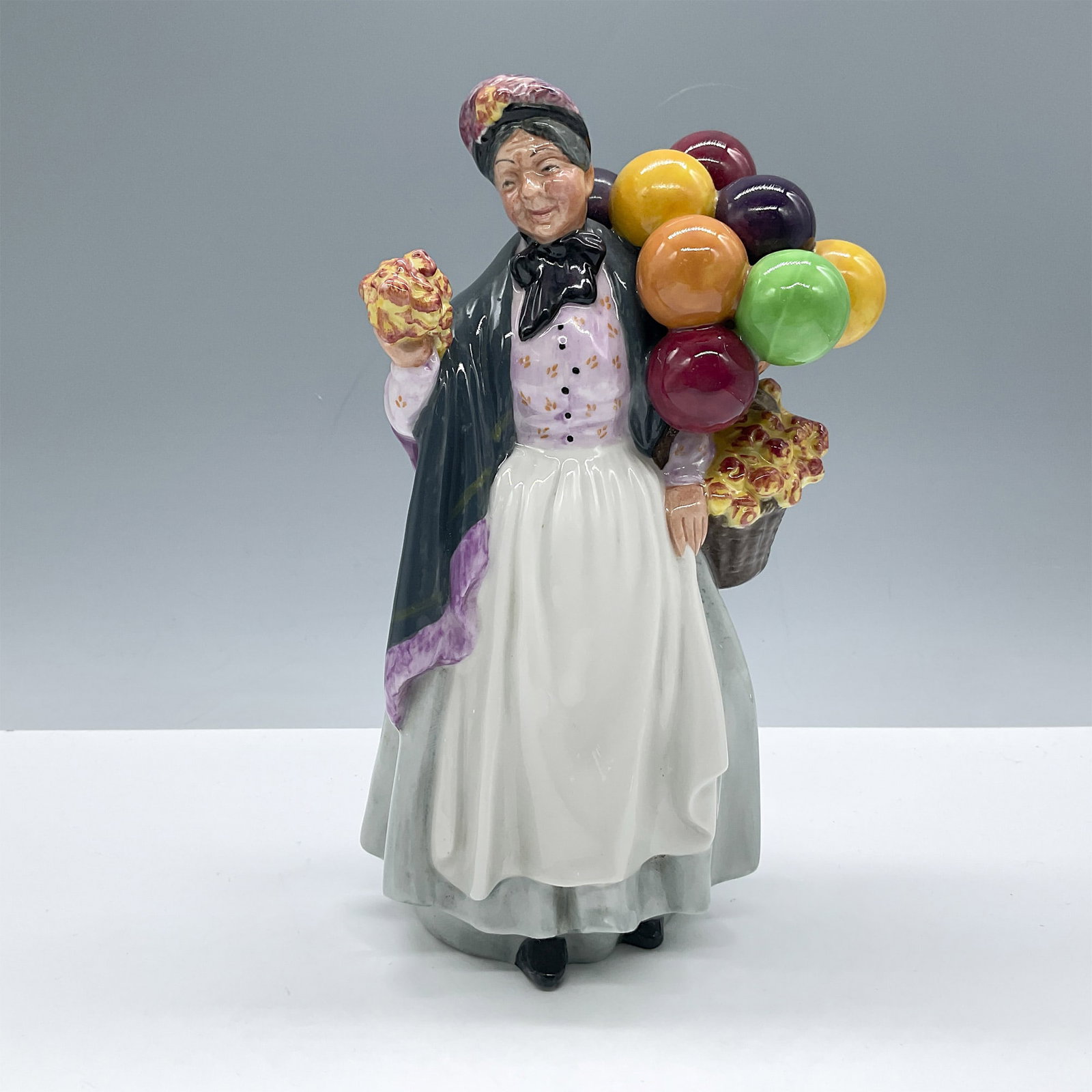 Biddy Pennyfarthing HN1843 - Royal Doulton Figurine: Glossy porcelain. From the Balloon Characters series. Features a lovely lady dressed in a purple blouse and gray shawl. Royal Doulton backstamp. Artist: Leslie Harradine Issued: 1938 - 2009 Dimensions