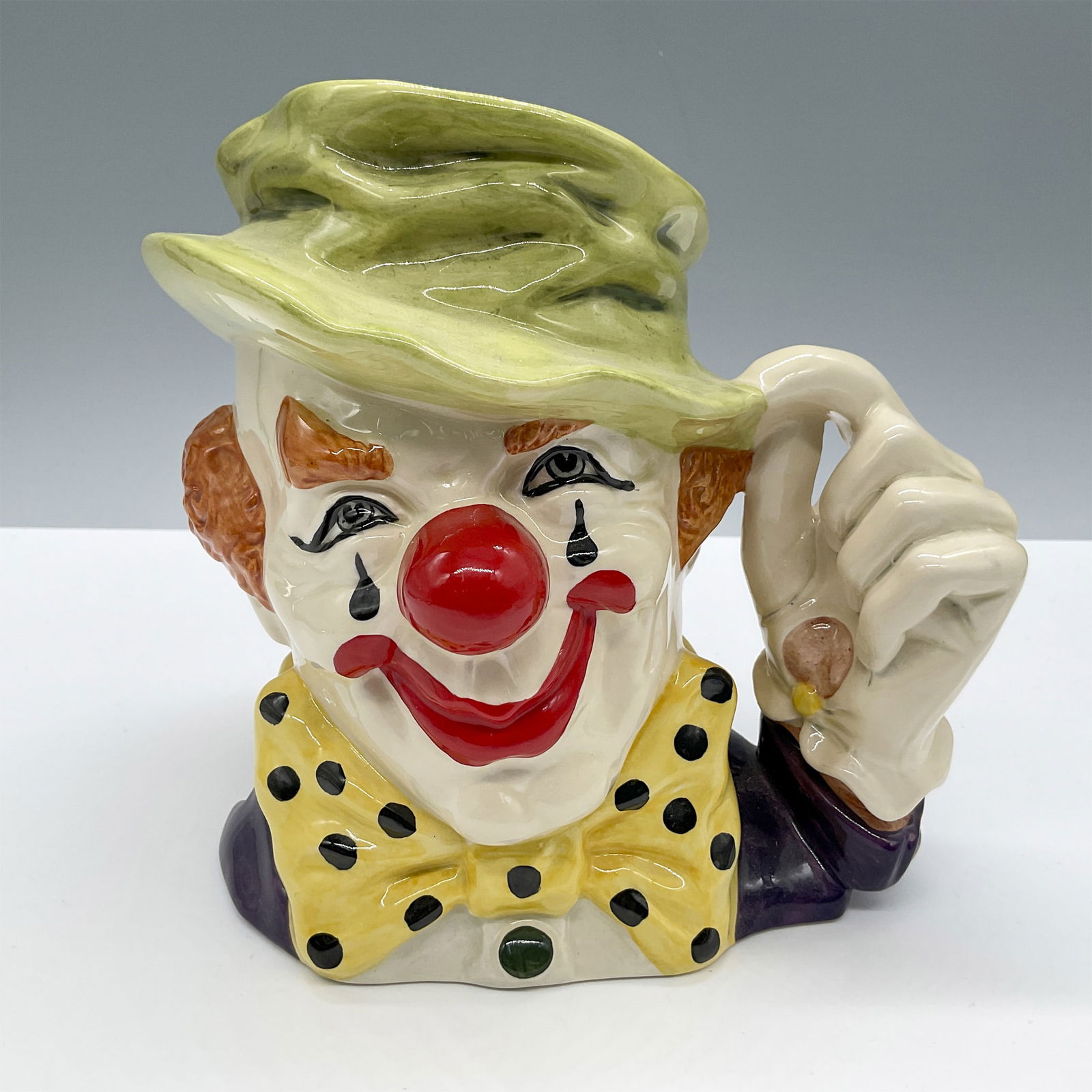 Clown D6834 - Large - Royal Doulton Character Jug: Style Two. Green cap, yellow bow tie with black spots, red nose and mouth. Royal Doulton backstamp. Artist: Stanley J. Taylor Issued: 1989 - 1995 Dimensions: 7"L x 5.5"W x 6.5"H Country of Origin: Eng