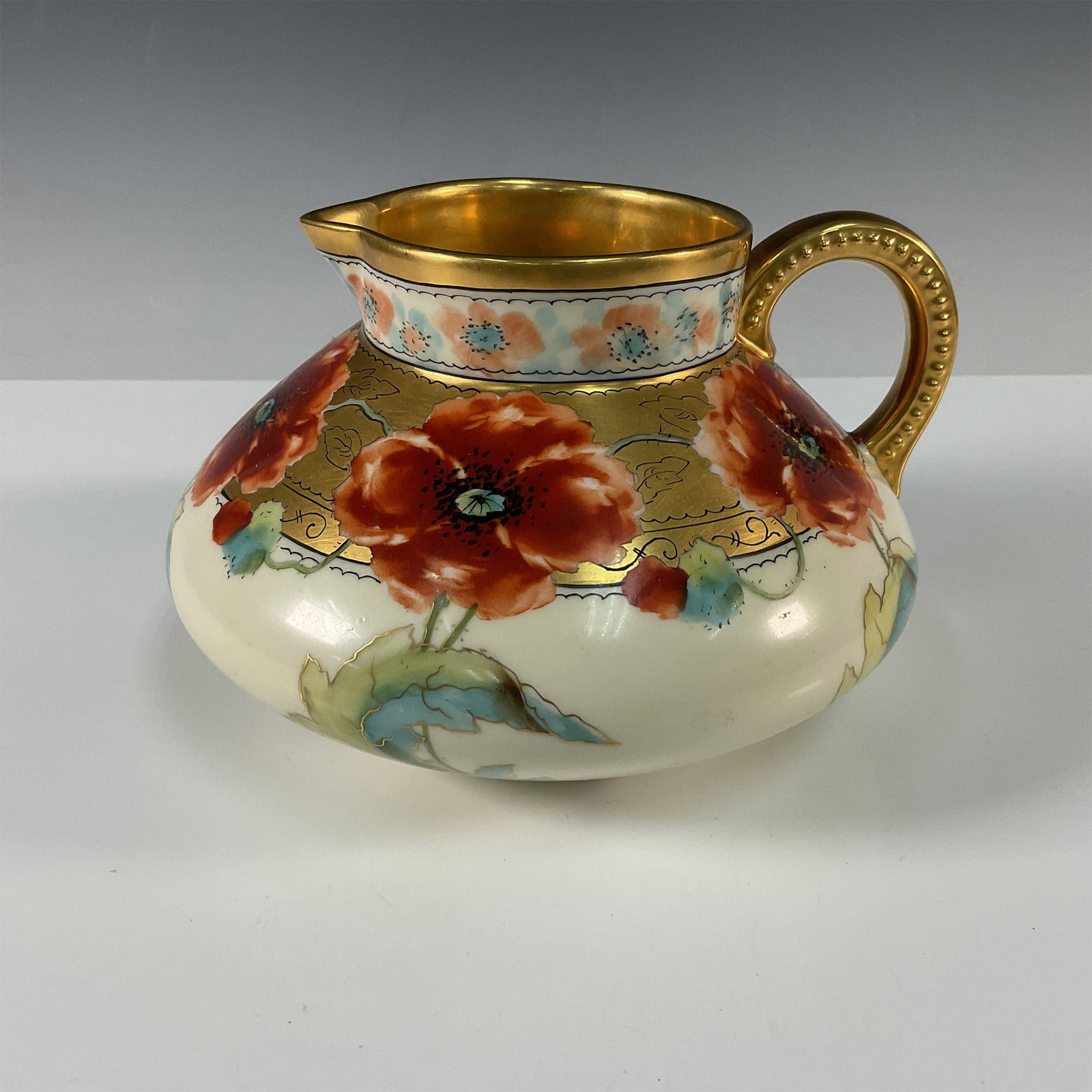Pickard Jean Pouyat Bone China Poppy Design Jug: A beautiful Pickard hand painted jug featuring poppies blossoms in shades of red, highlighted with gilt accents. The wide gold band at the top is intricately decorated with delicate patterns, adding a