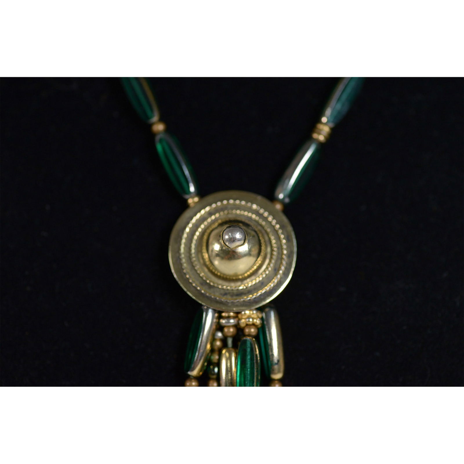 Beaded Necklace with Taxco Sterling Charms: An eclectic mixed-media necklace featuring deep green tubular beads interspersed with brass accents and various metallic elements. The necklace is adorned with an array of dangling brass charms, inclu