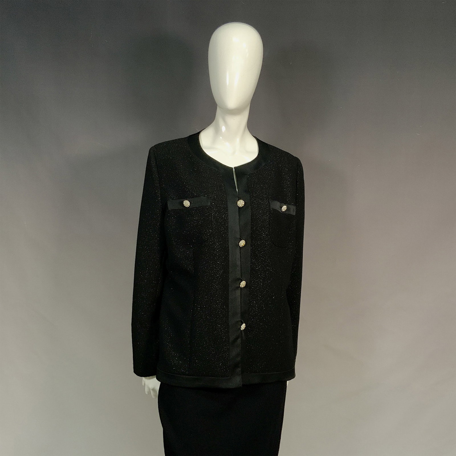 Marie Clemence Paris Black Round Neck Blazer: Structured silhouette blazer with collarless design and a subtle textured pattern. Features decorative buttons on the front and in the chest pockets. The piece is detailed with black satin trims aroun