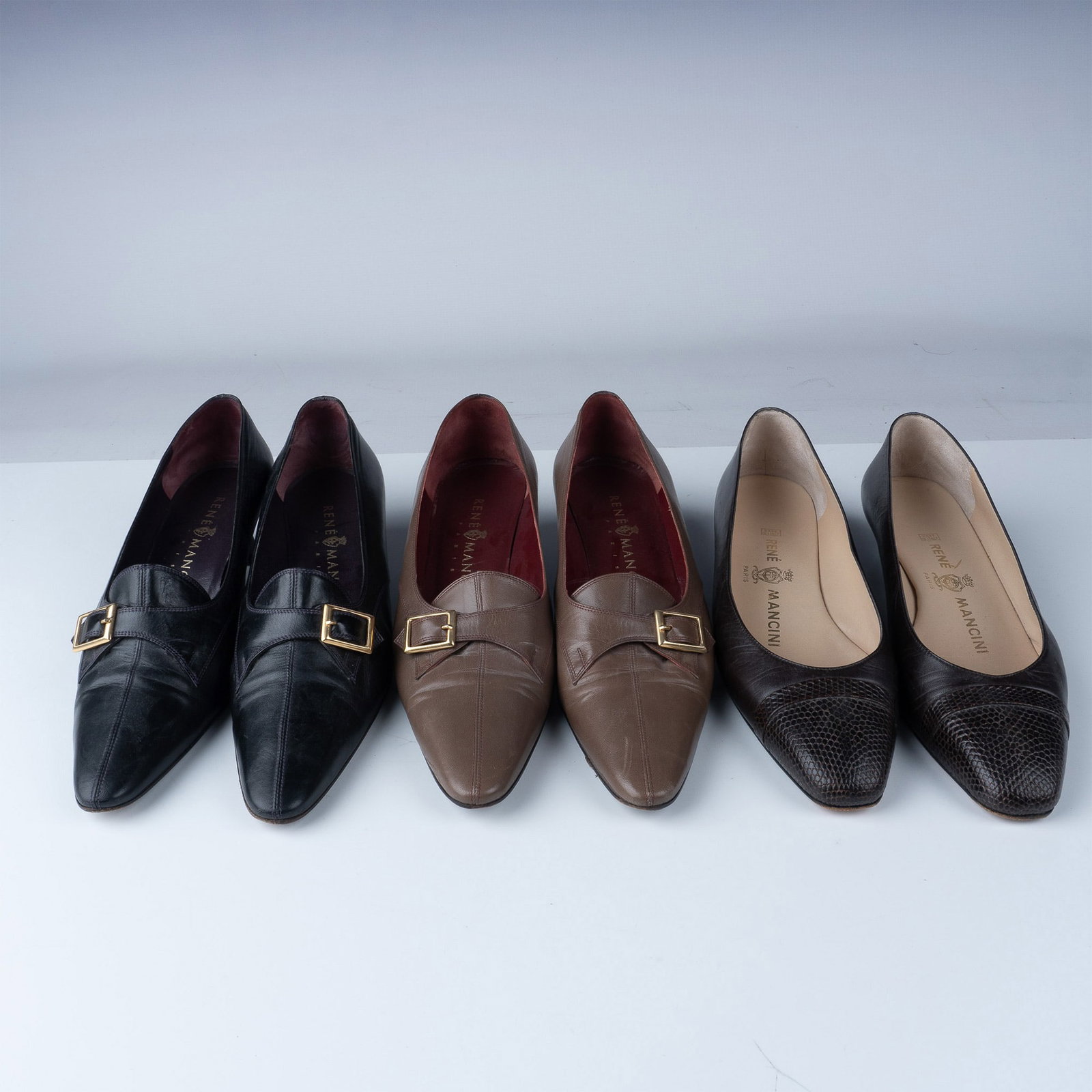 3 Pairs of Rene Mancini Leather Shoes: This lot includes three pairs of Rene Mancini leather shoes in size 39. One pair features brown leather with a gold-tone buckle detail, while two pairs are black leather with similar buckle designs. A