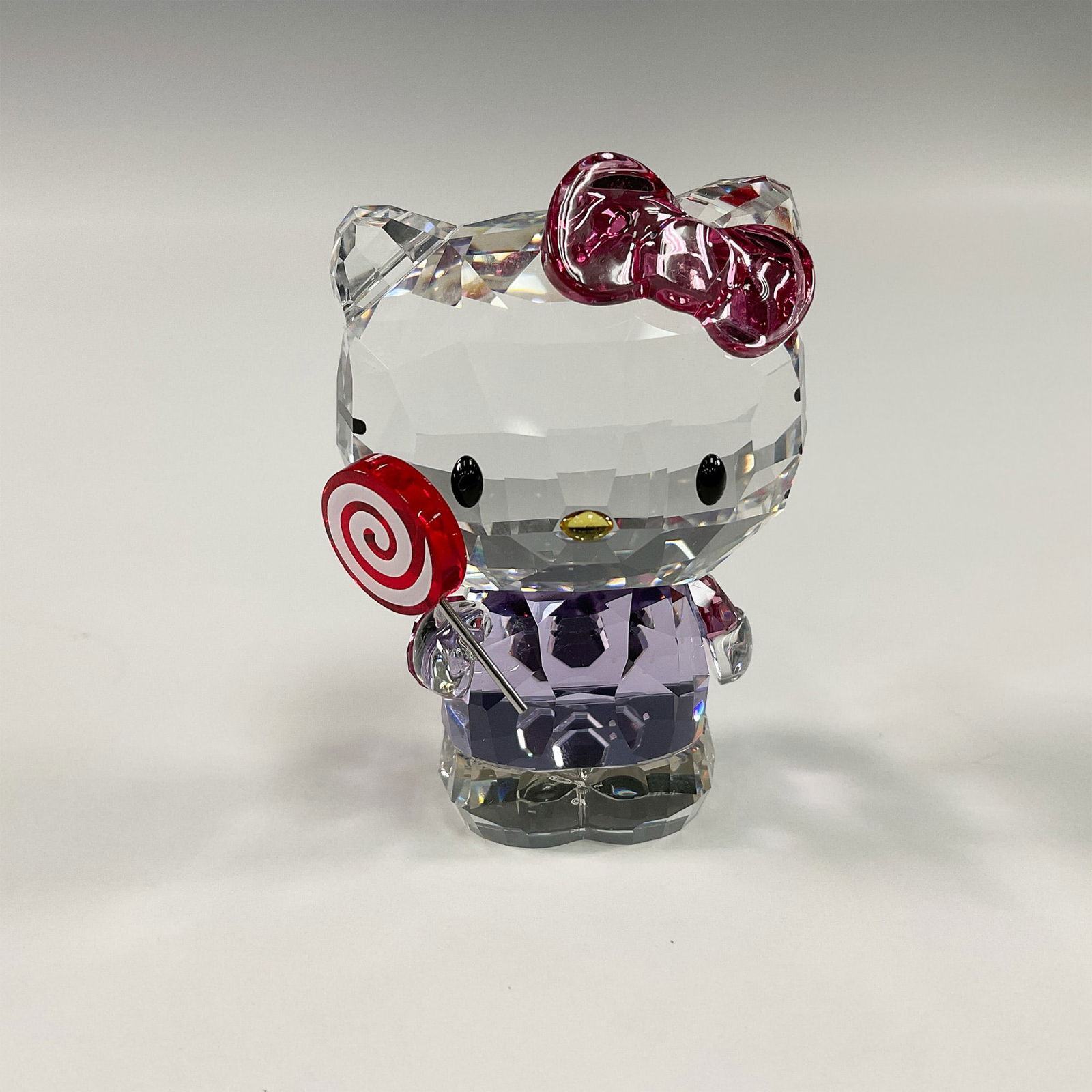 Swarovski Sanrio Crystal Figurine, Hello Kitty with Lollipop: A charming collaboration between Swarovski and Sanrio, this Hello Kitty crystal figurine captures the beloved character in a playful pose, holding a lollipop. Crafted from clear and colored Swarovski