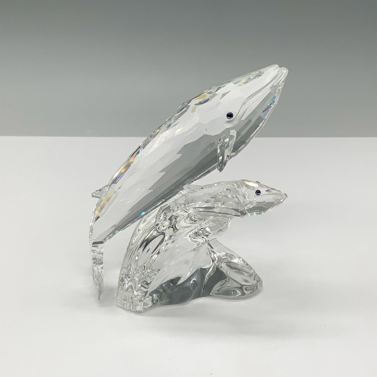 Swarovski Annual Edition Figurine, Care For Me The Whales: This Swarovski crystal sculpture, "Care For Me," features a mother and calf whale gliding together atop a crystal wave. Designed by Michael Stamey, it was introduced and retired in 1992 as part of Swa