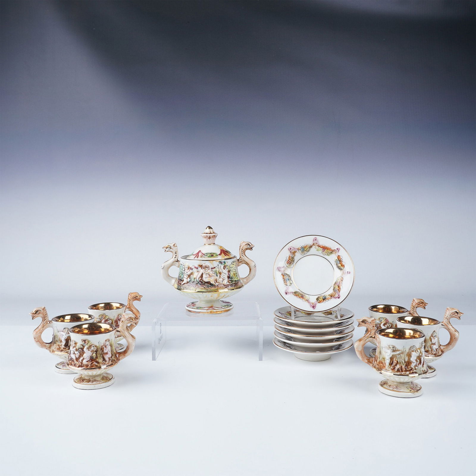 Capodimonte Porcelain Demitasse Set in Original Box: Elegant 13pc Capodimonte porcelain demitasse set, featuring six cups (3"H) with ornate handles, six saucers (4" dia.), and a matching lidded sugar bowl (4.5"H). Each piece showcases intricate raised-r