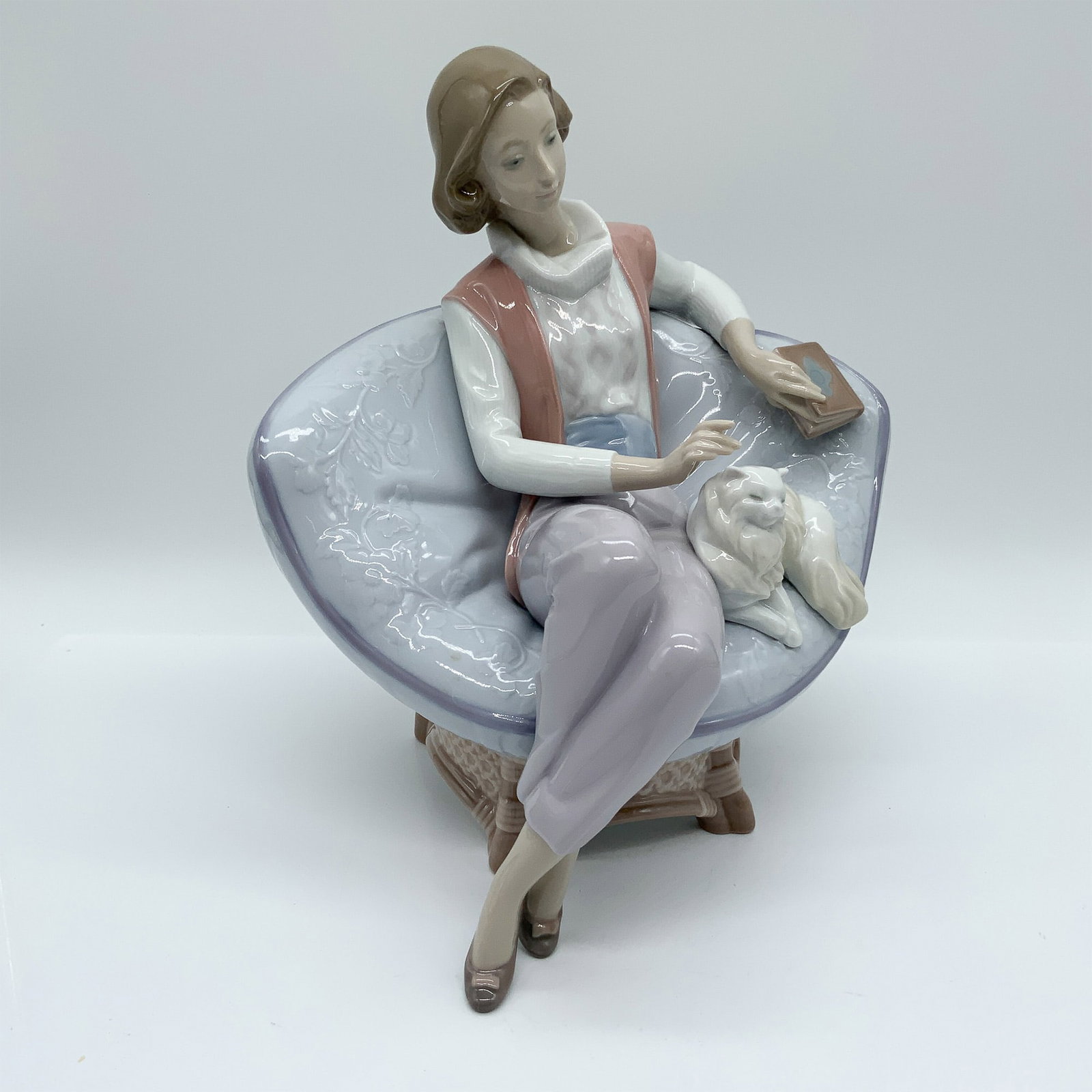 Lladro Porcelain Figurine ? A Quiet Evening, #6638: This Lladro figurine, A Quiet Evening (#6638), depicts a woman lounging in a plush chair, gently petting her cat while holding a book. Designed by Jos? Luis Alvarez, it showcases Lladro?s signature pa