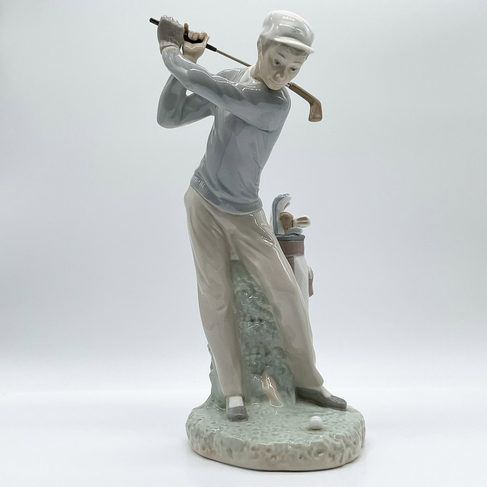 Lladro Porcelain Figurine, Golfer 1004824: This is a Lladro porcelain figurine titled Golfer, designed with intricate detail showcasing a golfer mid-swing. Produced in Spain, the figurine features a male golfer wearing a sweater and cap, accom
