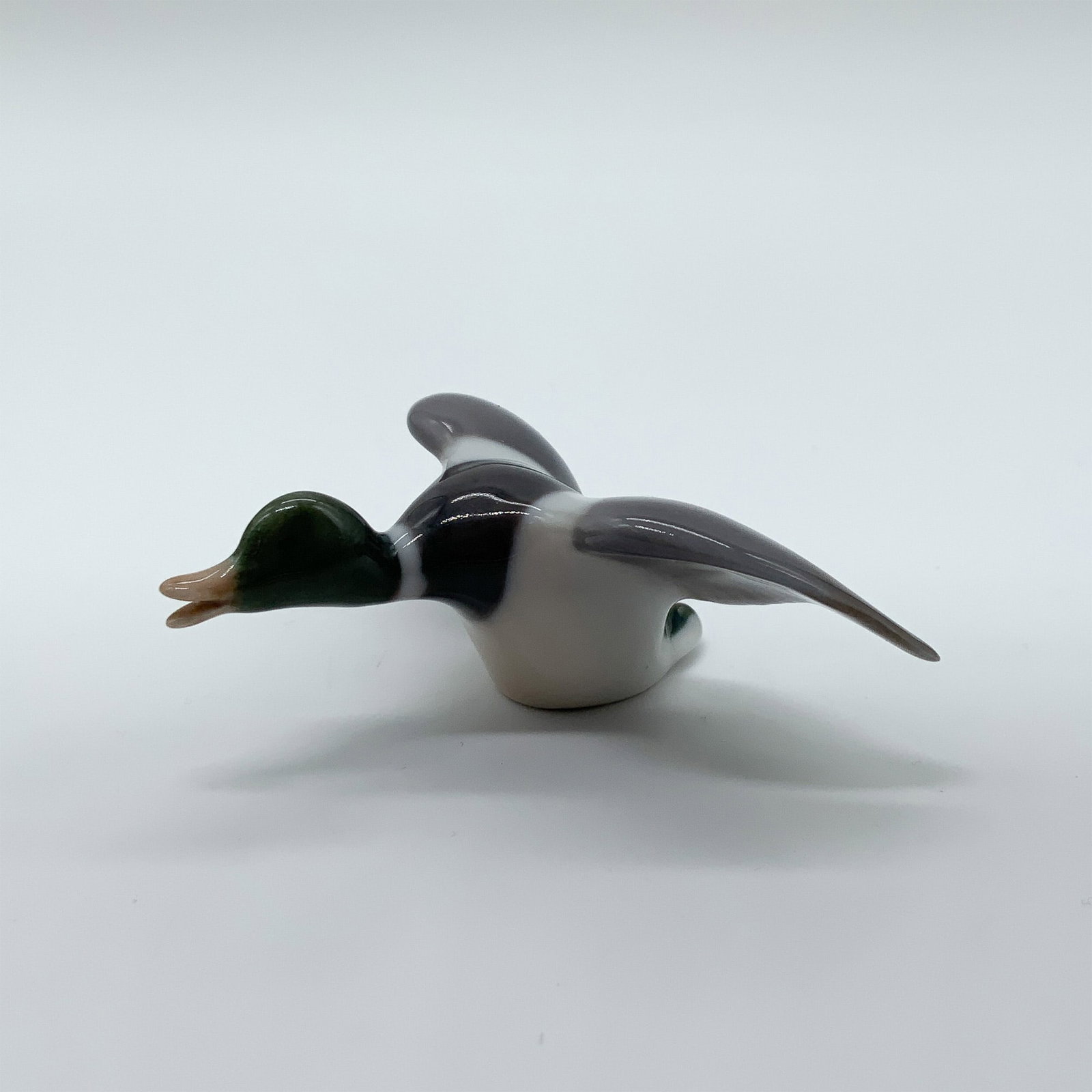 Bing & Grondahl Porcelain Flying Mallard Figurine: A finely detailed Bing & Grondahl porcelain figurine of a flying mallard, featuring a glossy finish and naturalistic coloring. Marked with the B&G backstamp for authenticity. Issued: 20th century Dime