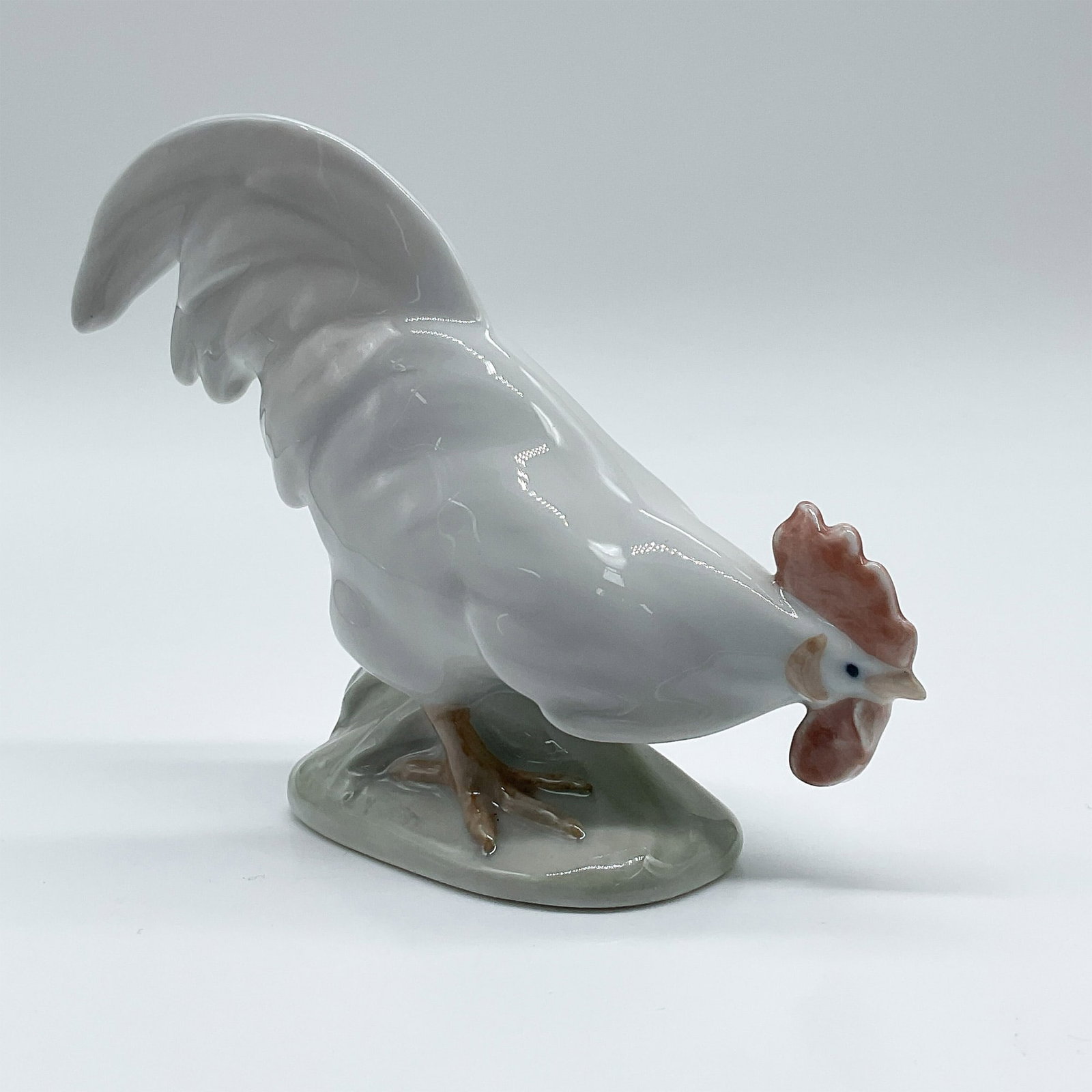 Royal Copenhagen Porcelain Figurine, Hen: This Royal Copenhagen porcelain figurine depicts a meticulously crafted hen in a dynamic pose. Model number 1127, the piece features detailed hand-painted elements, including a bright red comb and rea