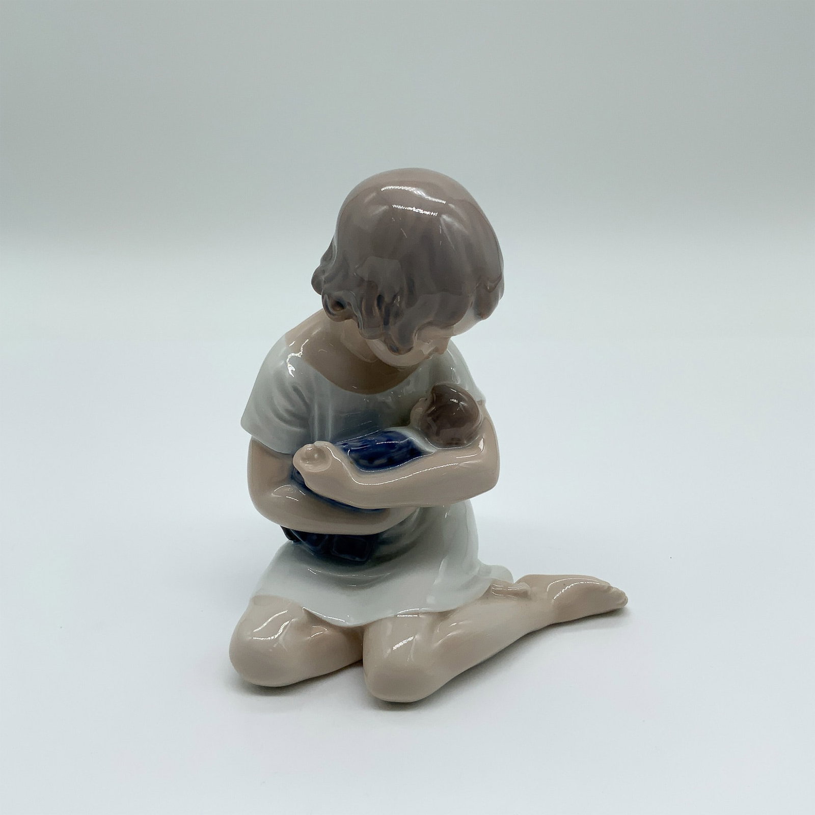 Royal Copenhagen Porcelain Figurine "Girl with Doll" 1938: Charming Royal Copenhagen porcelain figurine Girl with Doll (No. 1938), depicting a seated young girl tenderly cradling her doll. Finished in the brand?s signature soft glaze with pastel tones, showca
