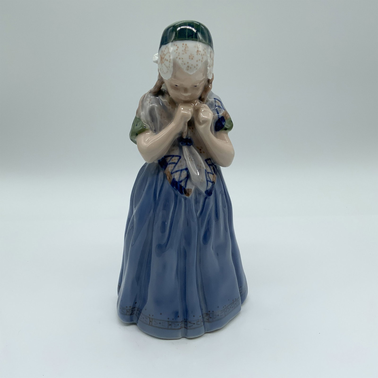 Royal Copenhagen Porcelain Figurine, Girl from Bornholm 1323: Royal Copenhagen porcelain figurine #1323, Girl from Bornholm, featuring a young girl in traditional attire with a blue dress, bonnet, and shawl. Beautifully hand-painted with delicate detailing, she 