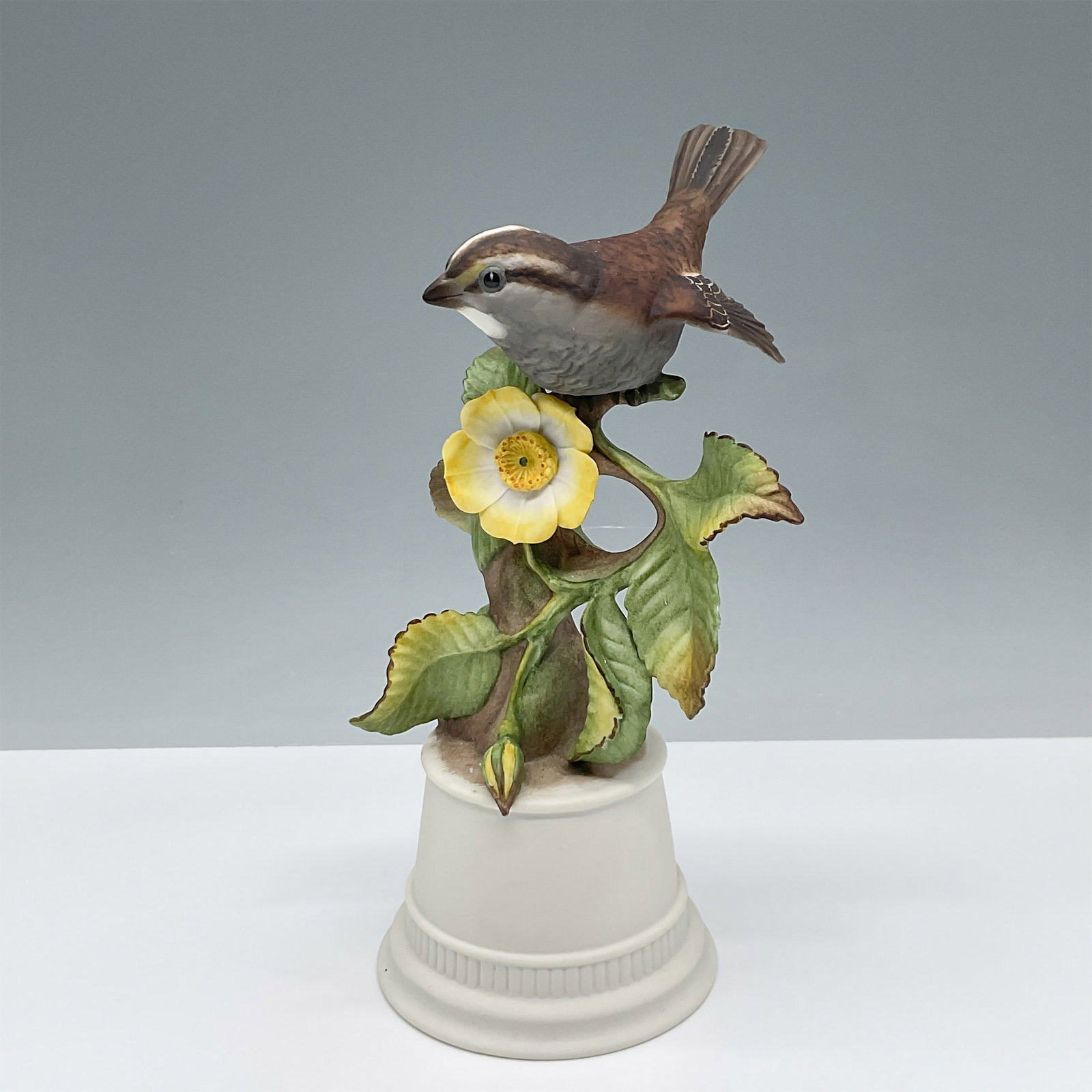 Boehm White-Throated Sparrow Porcelain Sculpture: This exquisitely crafted porcelain sculpture, created by the renowned Boehm Porcelain, features a lifelike depiction of a white-throated sparrow perched atop a flowering branch. The fine details of th