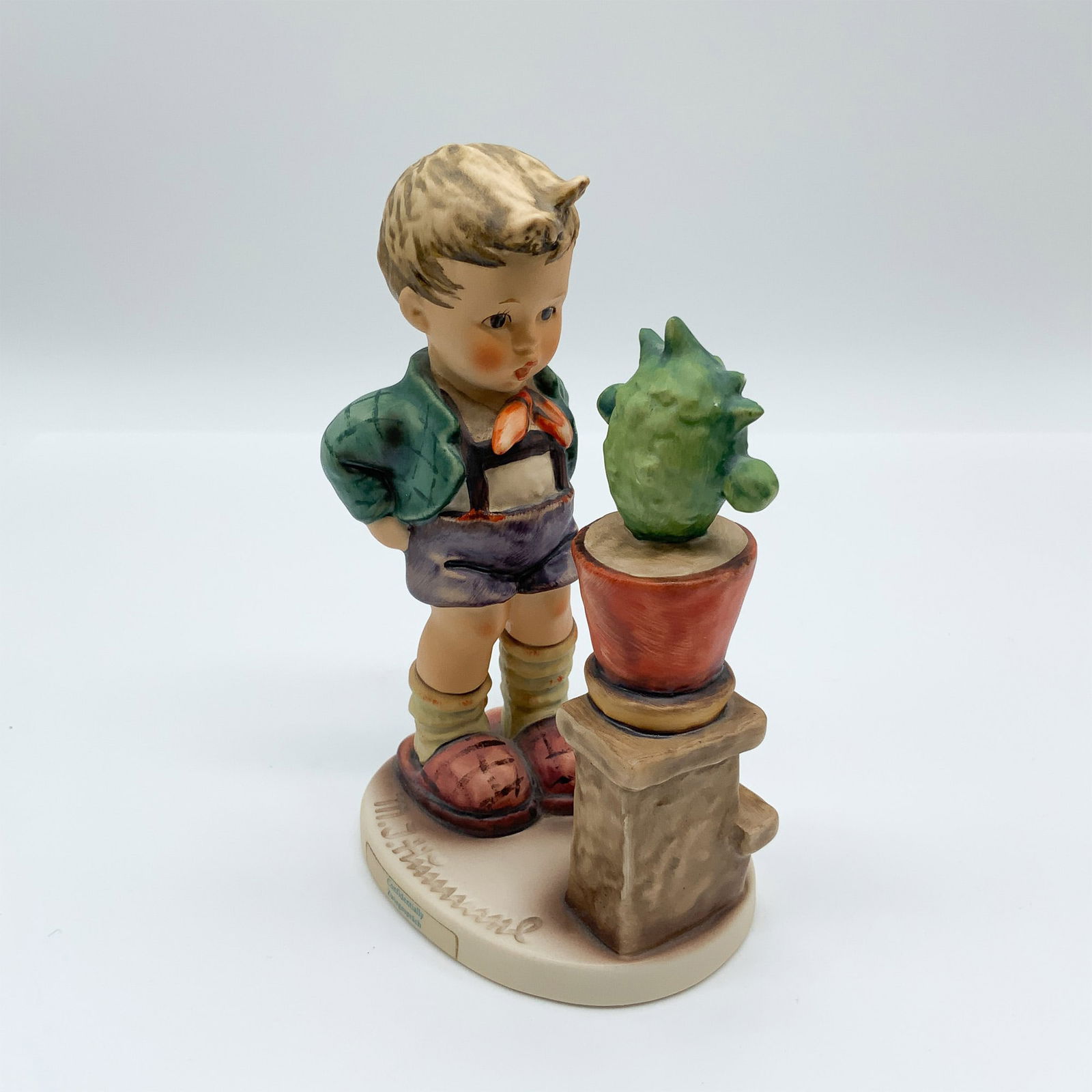 Goebel Hummel Porcelain Figurine, Confidentially HUM 314: Goebel Hummel figurine Confidentially (#314), featuring a young boy curiously inspecting a potted cactus. Marked with the Goebel backstamp and incised model number 314 on the base. Issued: 1979-1990 D