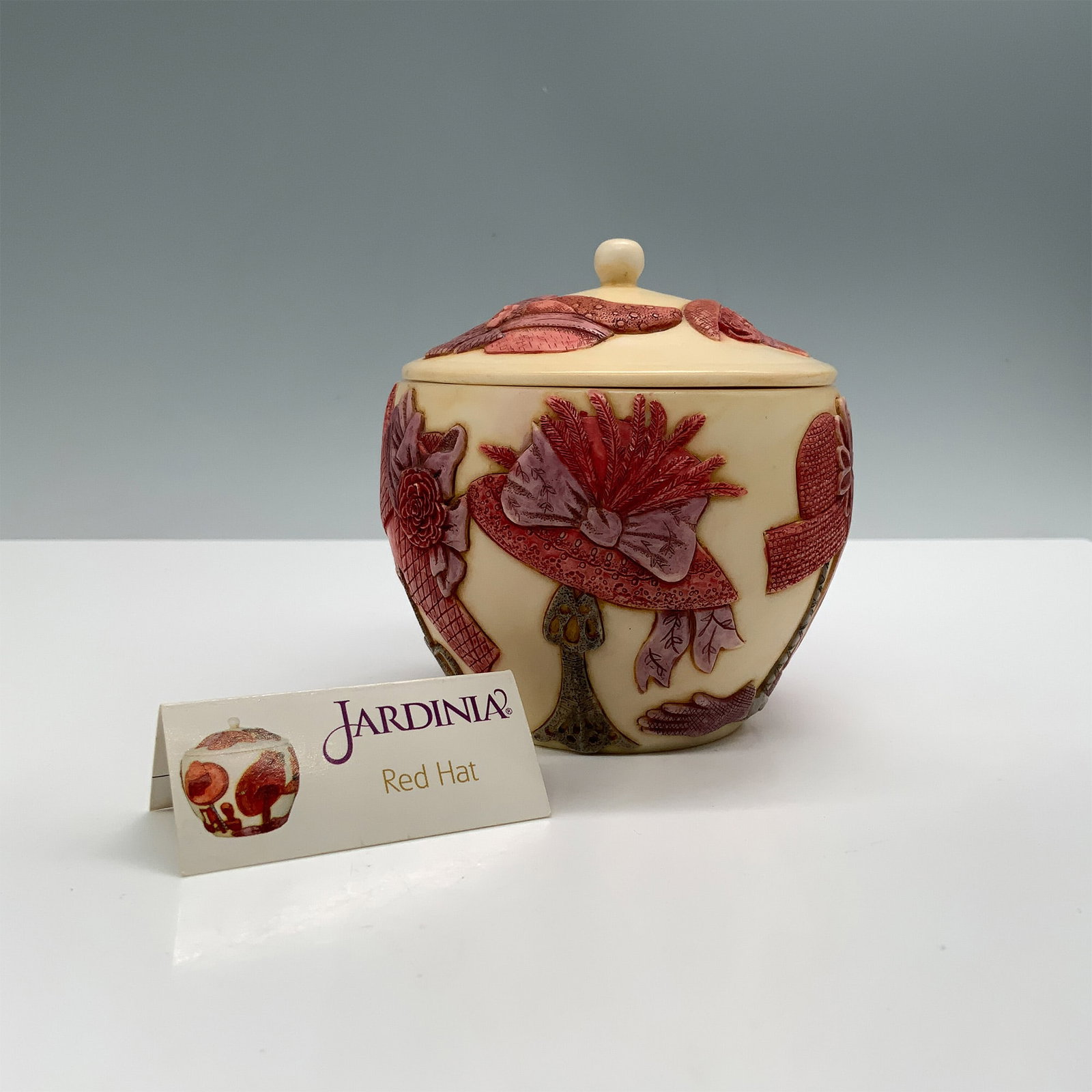 Harmony Ball Jardinia Red Hat Treasure Box: This Harmony Ball Treasure Box, titled Jardinia Red Hat, features intricate red and cream floral and hat motifs adorning its surface. The interior contains the French inscription, "Lorsque que je sera