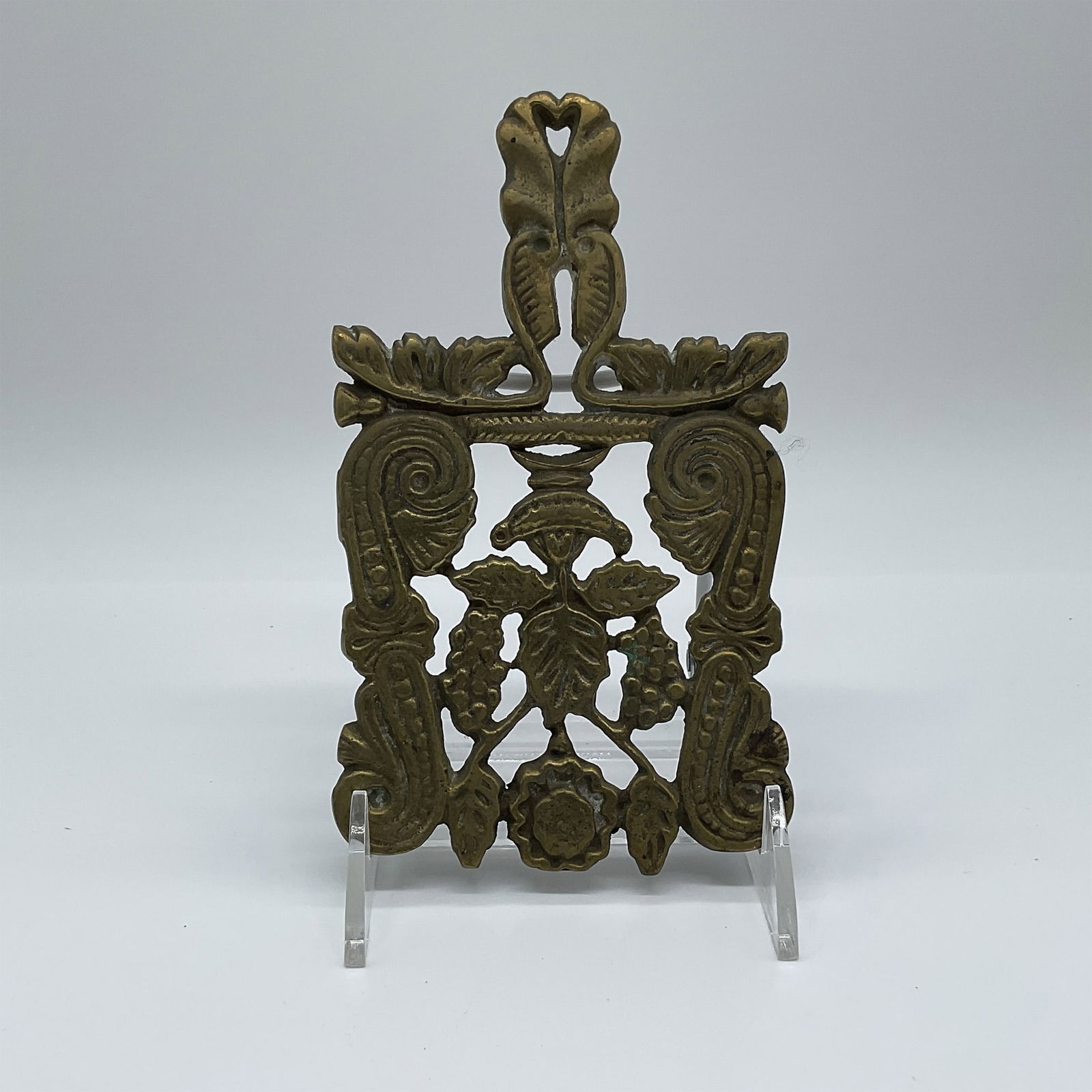 Cast Brass Trivet, Ornate Grape Motif: A vintage cast brass trivet featuring an intricate grapevine and scrollwork motif. This decorative piece showcases finely detailed craftsmanship with raised floral and leaf elements, adding an elegant