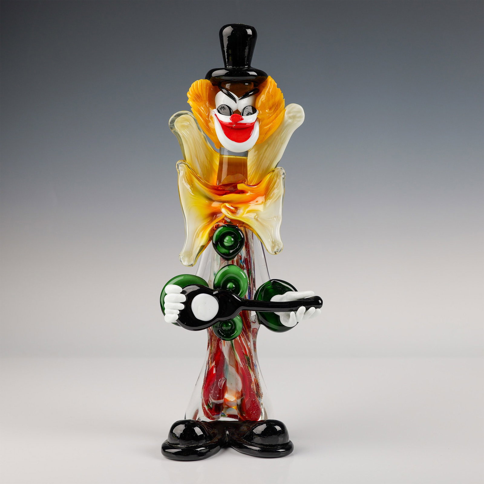 Murano Glass Clown Figurine with Guitar: This striking Murano glass clown figurine stands 12.5''H and showcases vibrant colors and intricate detailing, characteristic of high-quality Murano craftsmanship. The clown, adorned with a yellow and