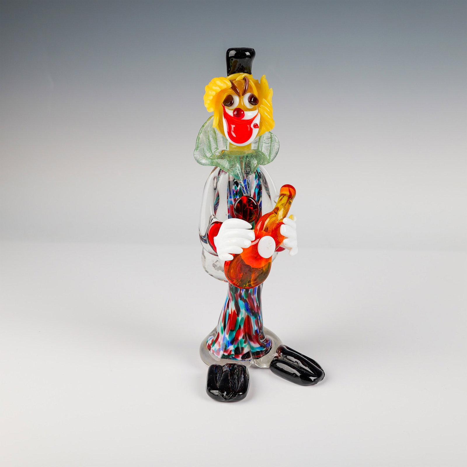 Murano Glass Clown Figurine with Guitar: A vibrant hand-blown Murano glass clown figurine, featuring a multicolored body with intricate patterns and a cheerful expression. The clown is depicted holding a detailed amber-colored guitar, showca