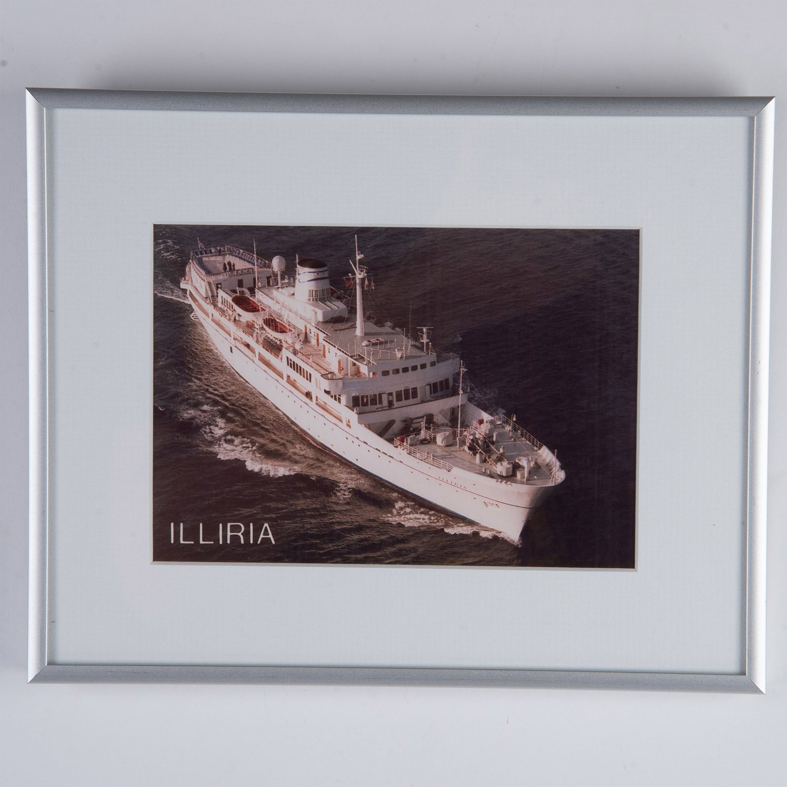 Original Color Photograph on Paper, Illiria Cruise Ship: Original color photograph on paper featuring the cruise ship Illiria at sea. Housed in a brushed silver metallic frame with a white mat. Sight size: 6.75"L x 4.75"H. Frame dimensions: 10.25"L x 8.25"H