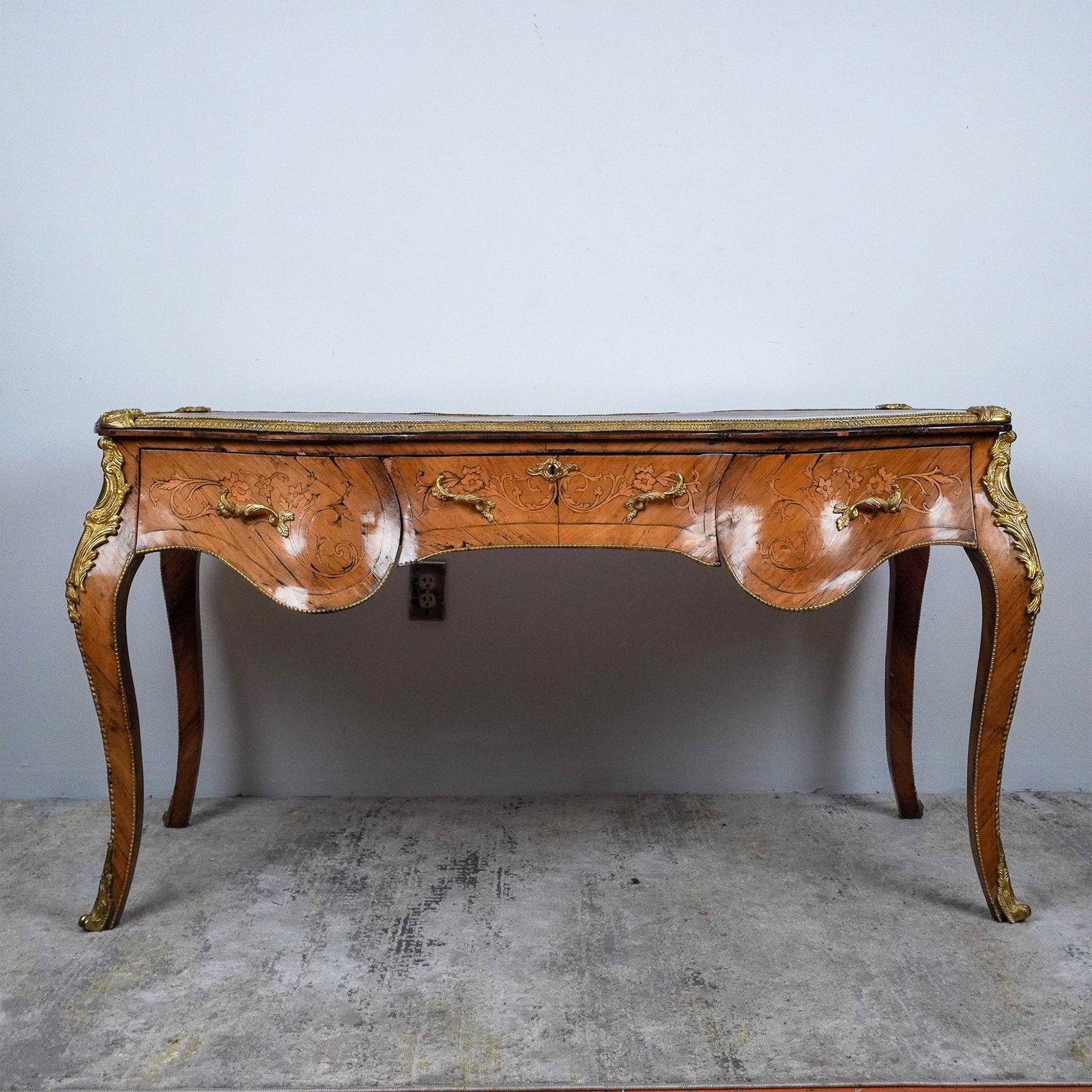 19th Century Louis XV-Style Serpentine-Shaped Writing Desk: This elegant writing desk that includes three large drawers is crafted in the Louis XV style and features a serpentine-shaped top with a red faux-leather writing surface bordered by intricate gilt too