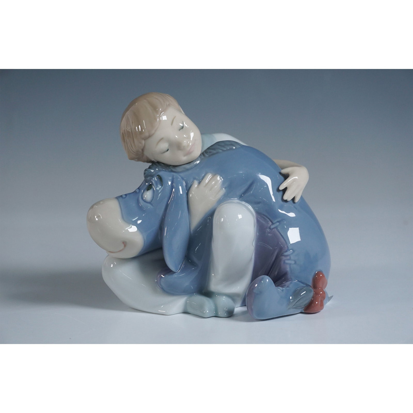 Nao by Lladro Disney Figurine, Dreams With Eeyore: This delightful porcelain figurine features a young child embracing Eeyore, the beloved character from Disney's Winnie the Pooh. Designed with exceptional craftsmanship, this piece showcases soft past