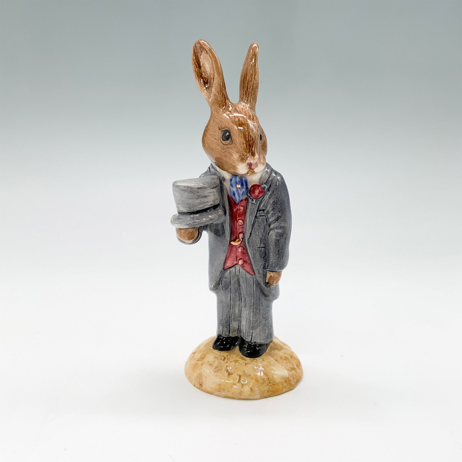 Royal Doulton Bunnykins Figurine Room DB102: Royal Doulton Bunnykins porcelain figurine titled Room Bunnykins, model number DB102. This charming piece features a Bunnykins character dressed in a formal suit, holding a cup, and standing on a text