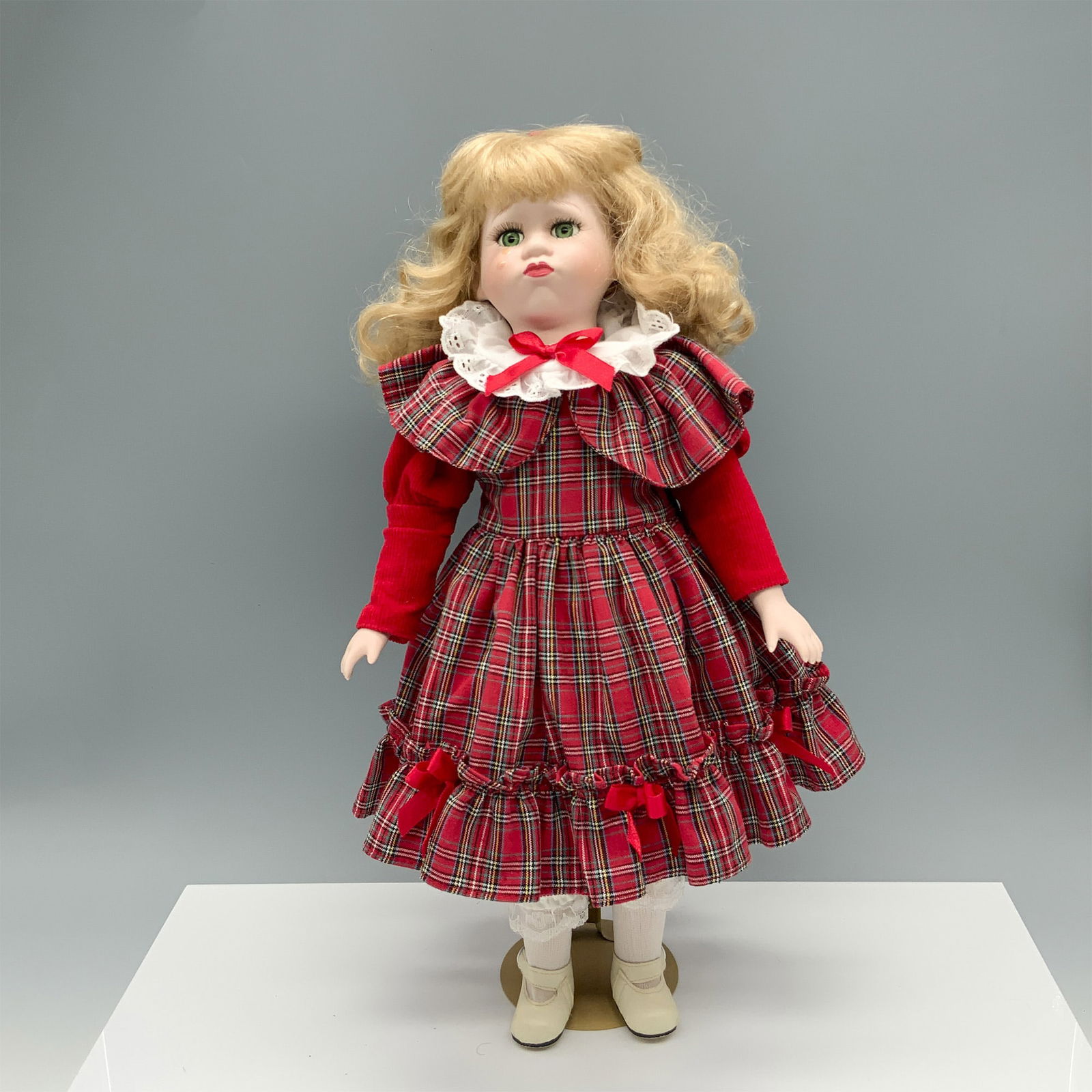 Teary Eyed Girl in a Plaid Dress Porcelain Doll: Cute green eyed blonde young girl modeling a red dress with ribboned bows on it. Metal stand included. Dimensions: 8.25"L x 7.5"W x 16"H