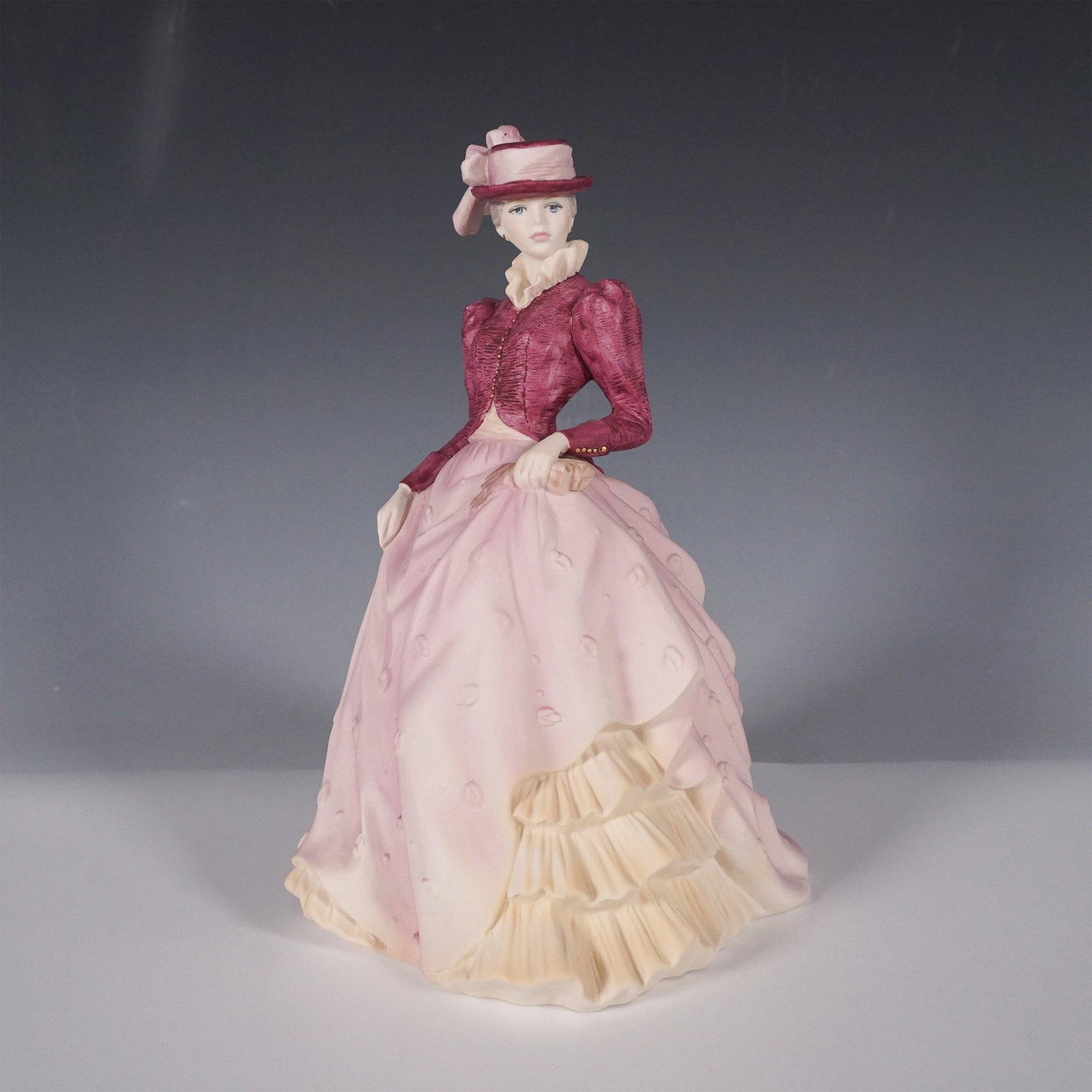 Coalport Age of Elegance Figurine, Hyde Park: Elegant porcelain figurine from the Age of Elegance collection. This refined piece depicts a lady dressed in a Victorian-inspired ensemble, featuring a burgundy textured jacket with gold button detail