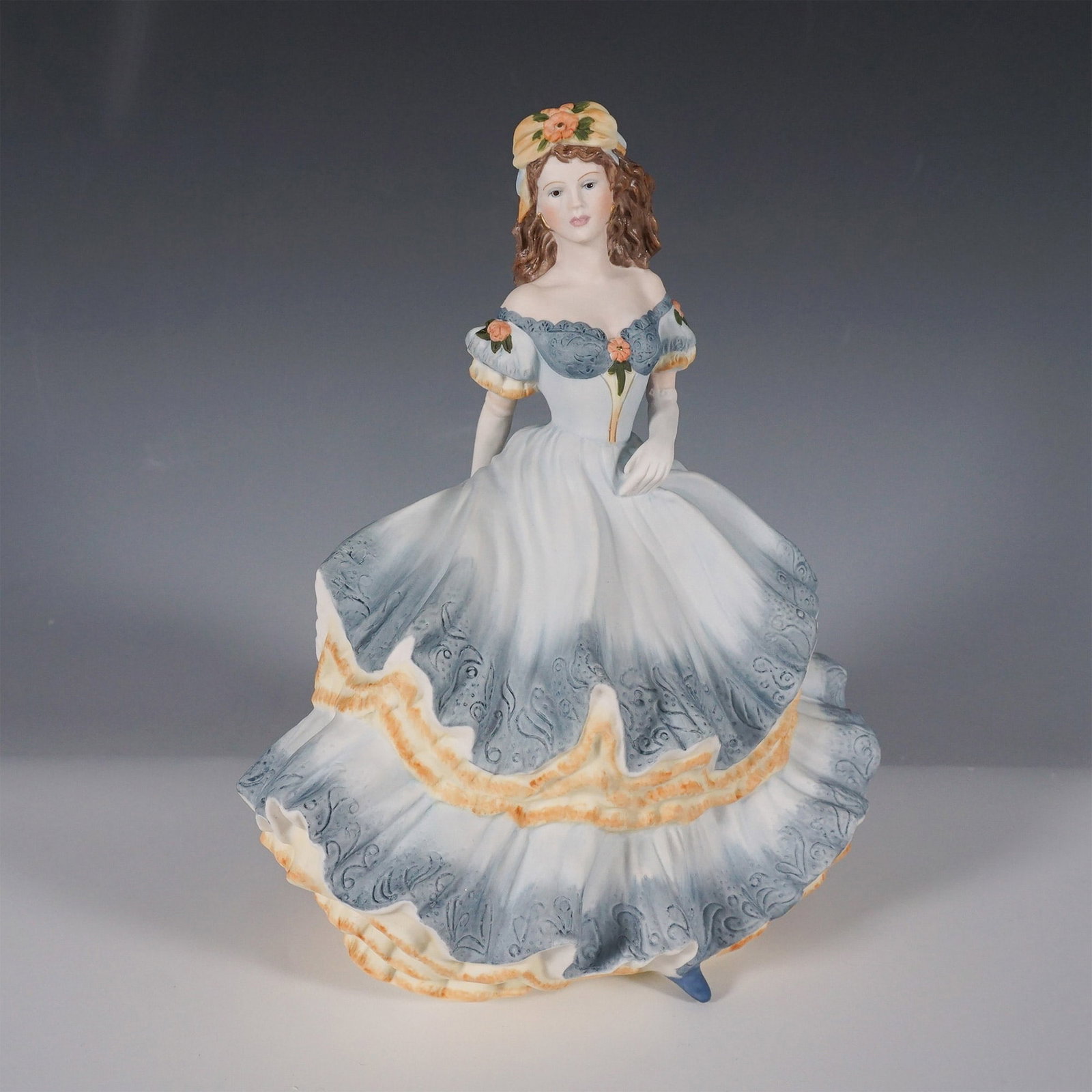 Coalport Age of Elegance Figurine, Secret Rendezvous: This exquisite porcelain figurine from Coalport's Age of Elegance collection. This hand-decorated piece captures the refined grace of a woman in a flowing blue and ivory gown adorned with intricate de