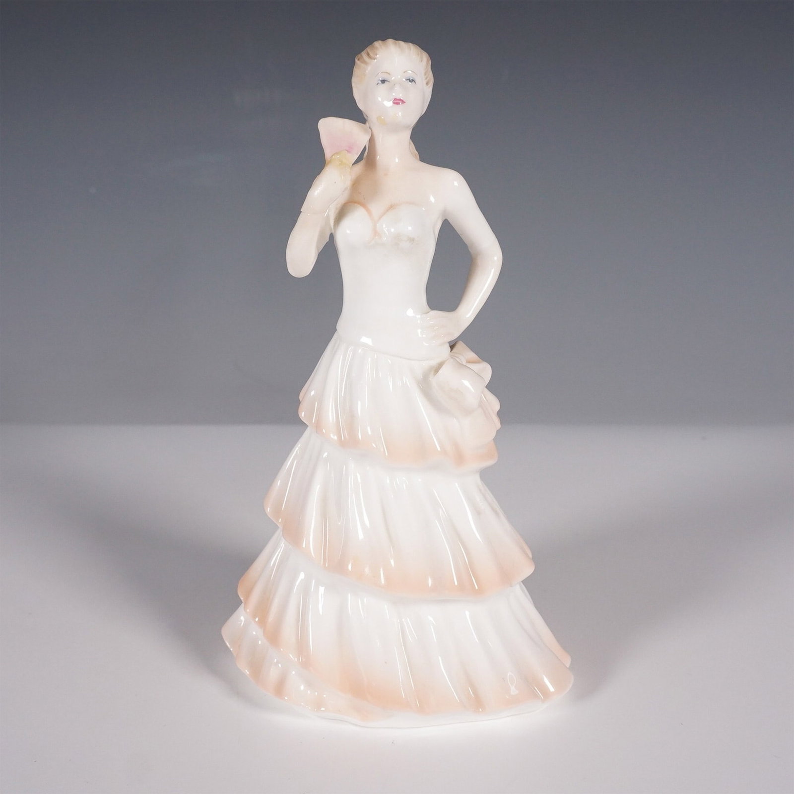 Coalport Porcelain Figurine, Katie: A Coalport figurine titled Katie from the "Katie" series, designed by John Bromley and decorated by hand. The piece features a lovely woman in a flowing gown, holding a delicate flower in one hand. Th