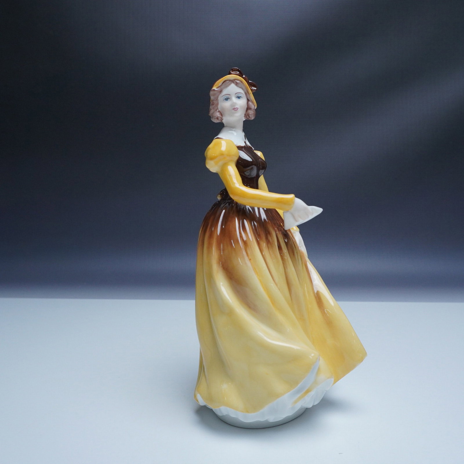 Coalport Ladies of Fashion Letter from a Lover Figurine: Charming Coalport porcelain figurine titled Letter from a Lover from the Ladies of Fashion collection. This hand-painted figurine depicts a refined lady in a flowing golden-yellow and brown gown, grac