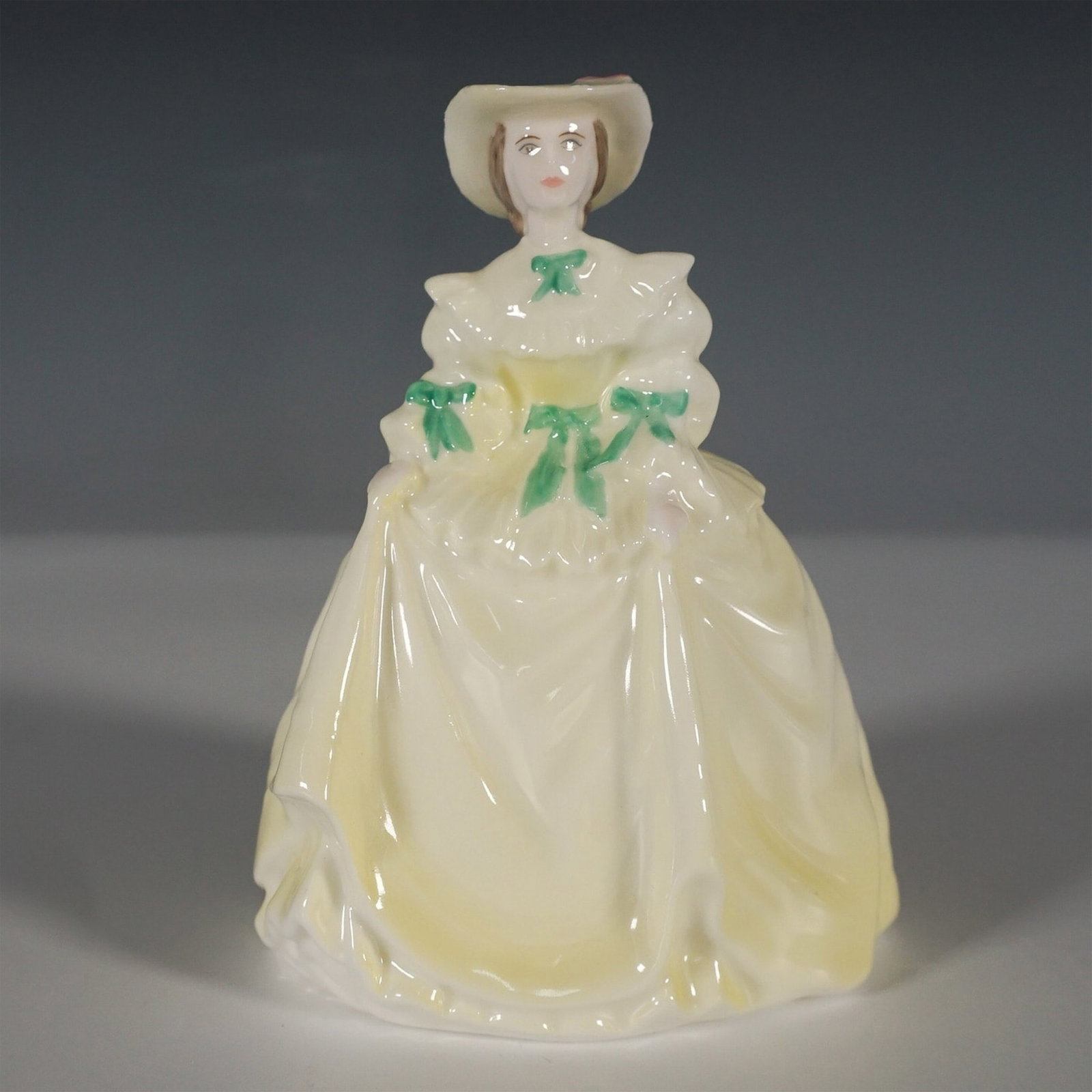 Coalport Porcelain Figurine, Springtime: A charming Coalport bone china figurine titled Springtime, featuring a finely detailed young woman in an elegant flowing gown with soft yellow hues and green ribbon accents. She wears a wide-brimmed h