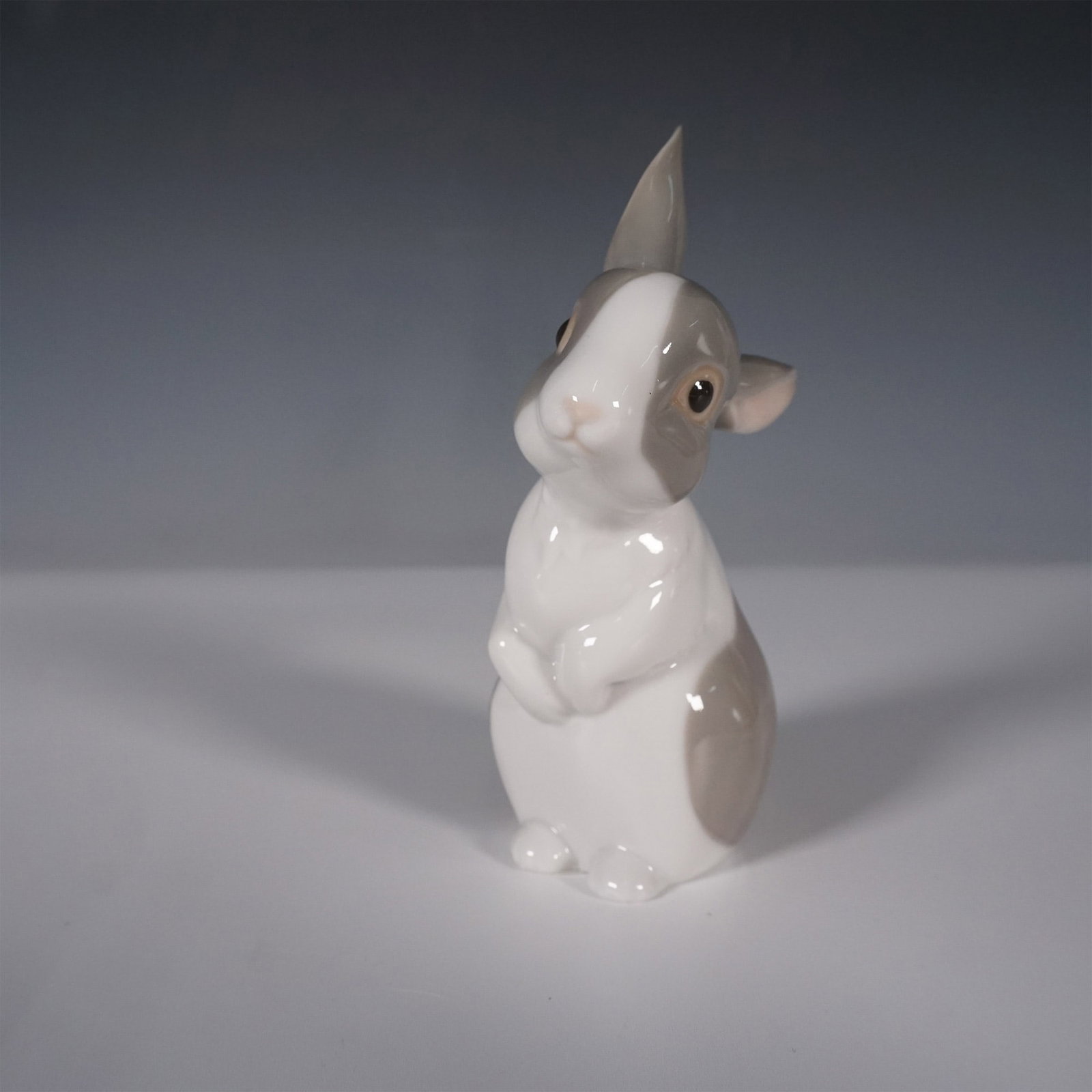 Nao by Lladro Figurine, Bunny with Original Egg Packaging: Nao by Lladro porcelain figurine featuring an endearing bunny in a lifelike seated pose with detailed hand-painted accents in white and gray. Crafted in Spain, this charming piece showcases the brand'