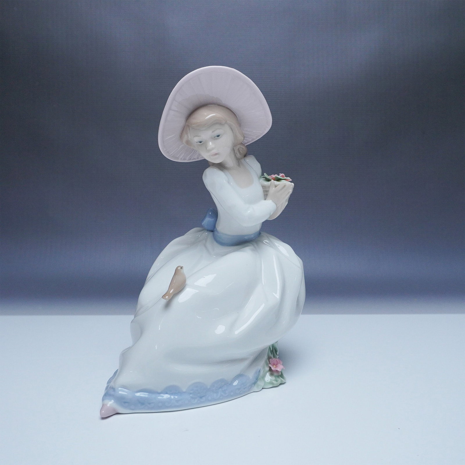 Nao by Lladro Figurine, The Nightingales Song 1345: Beautiful Nao by Lladro porcelain figurine titled The Nightingales Song, model number 1345. This elegant piece features a young girl in a flowing white dress with a soft blue trim, seated gracefully w
