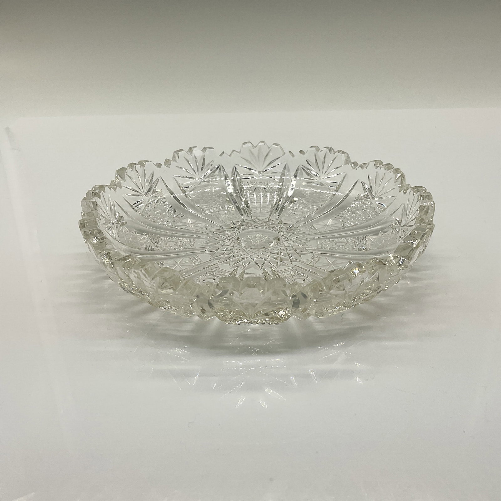Crystal Hand Cut Dish, Queen Lace Style: A beautiful small, scalloped edge dish with slightly raised sides and decorated with hobnails, stars, fans, and cross patterns. Issued: 20th century Dimensions: 1.75"H x 5.25"Dia.