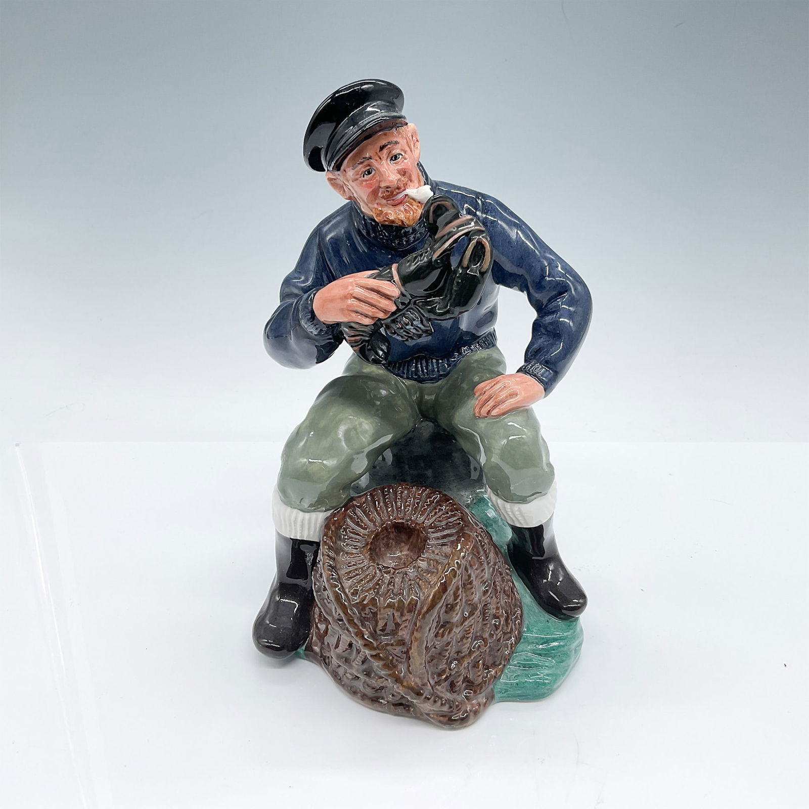 The Lobster Man HN2317 - Royal Doulton Figurine: This Royal Doulton figurine, titled "The Lobster Man," features a charming depiction of a sailor holding a lobster while seated beside a basket. Designed by Mary Nicoll and issued between 1964 and 199