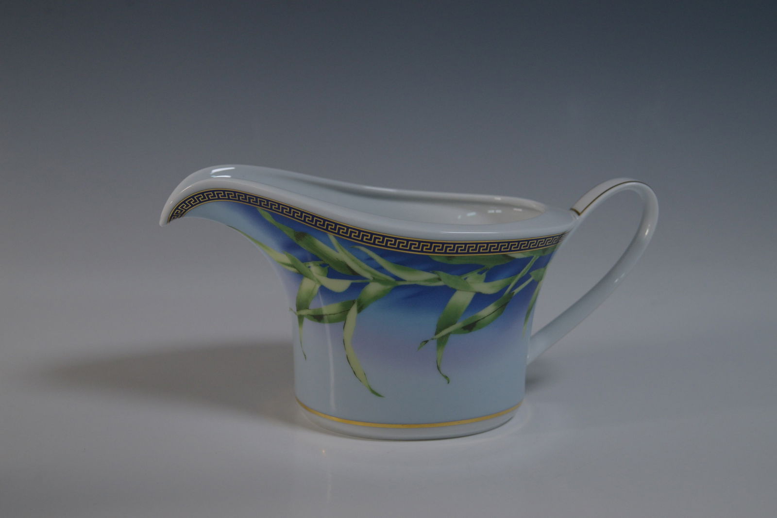 Rosenthal Versace Jungle Gravy Boat: Rosenthal Versace Jungle porcelain gravy boat. This elegant piece features a vibrant botanical design on a blue gradient background, accentuated with a Greek key border in gold. Marked on the undersid