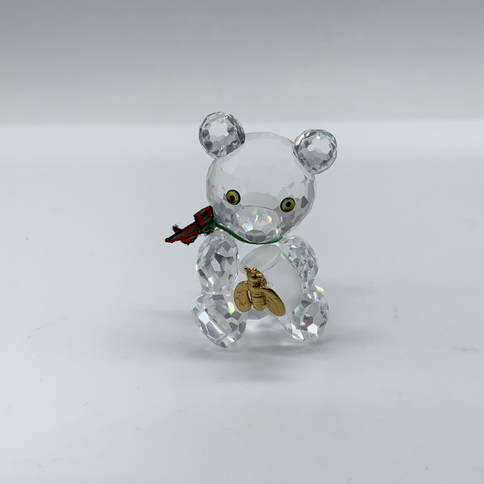 Swarovski Crystal Figurine, Kris Bear with Honey Pot: Charming crystal clear faceted figure that depicts Kris Bear with a green and red ribbon around his neck as he holds a frosted honey pot with a gold toned bee. This figure was part of the When We Were