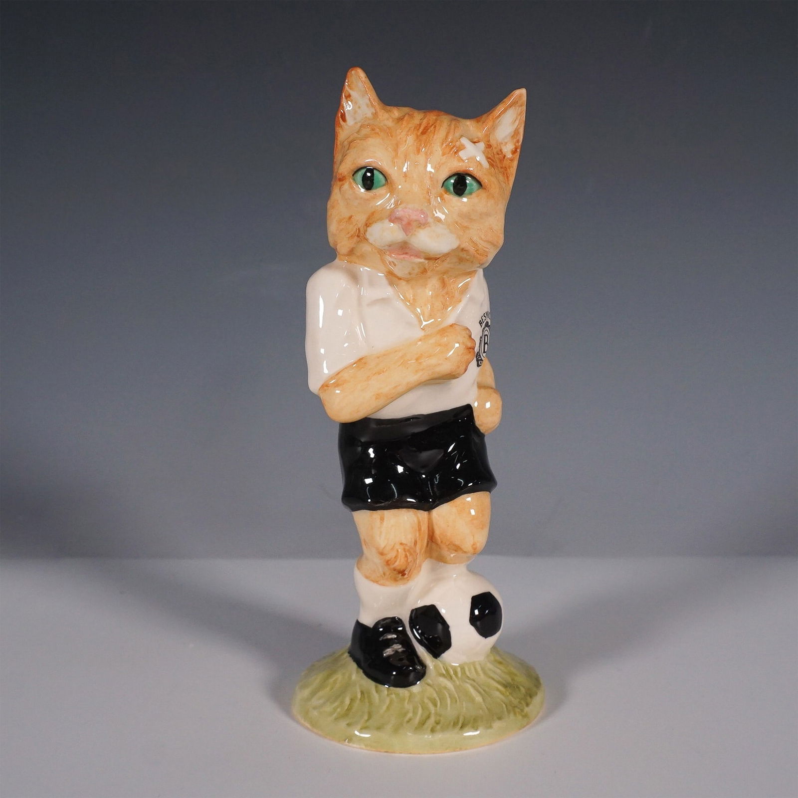 Beswick Footballing Felines Dribble Figurine: This delightful figurine from the Beswick Footballing Felines Collection is titled Dribble?and features a playful cat in a football uniform, confidently posing with a soccer ball at its feet. Made in