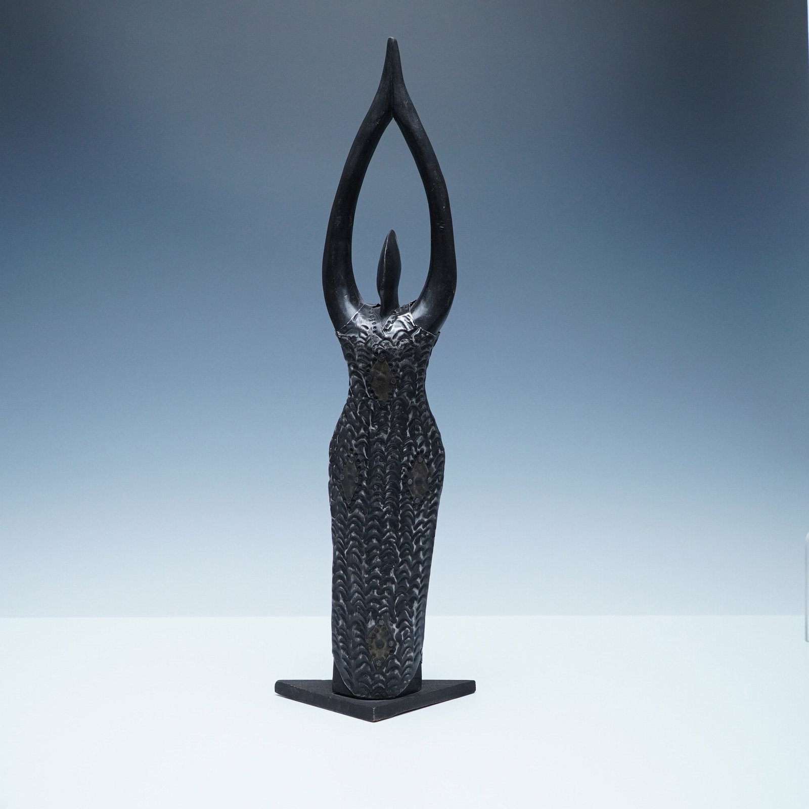 Ghanaian Handcrafted Wooden Sculpture with Hammered Metal Dress: A striking handcrafted sculpture from Ghana, featuring an elongated female form with arms raised in a graceful pose. The body is carved from wood, while the intricately textured dress is made of hamme